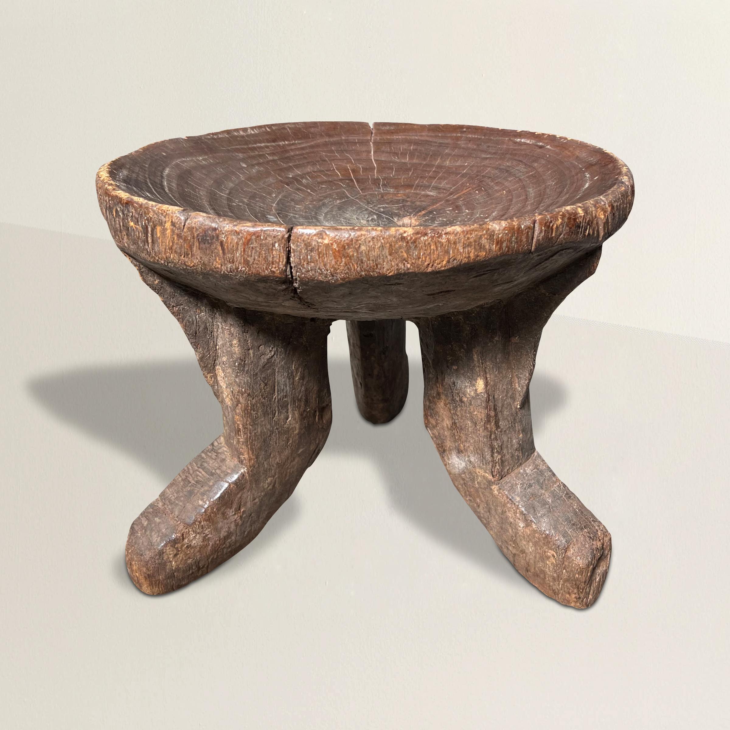 A wonderfully sculptural early 20th century Ethiopian stool from the Gurage Peoples, carved of one piece of wood with the most wonderful texture, and with three curved legs supporting a convex bowl-form seat with a natural knot in the center and a