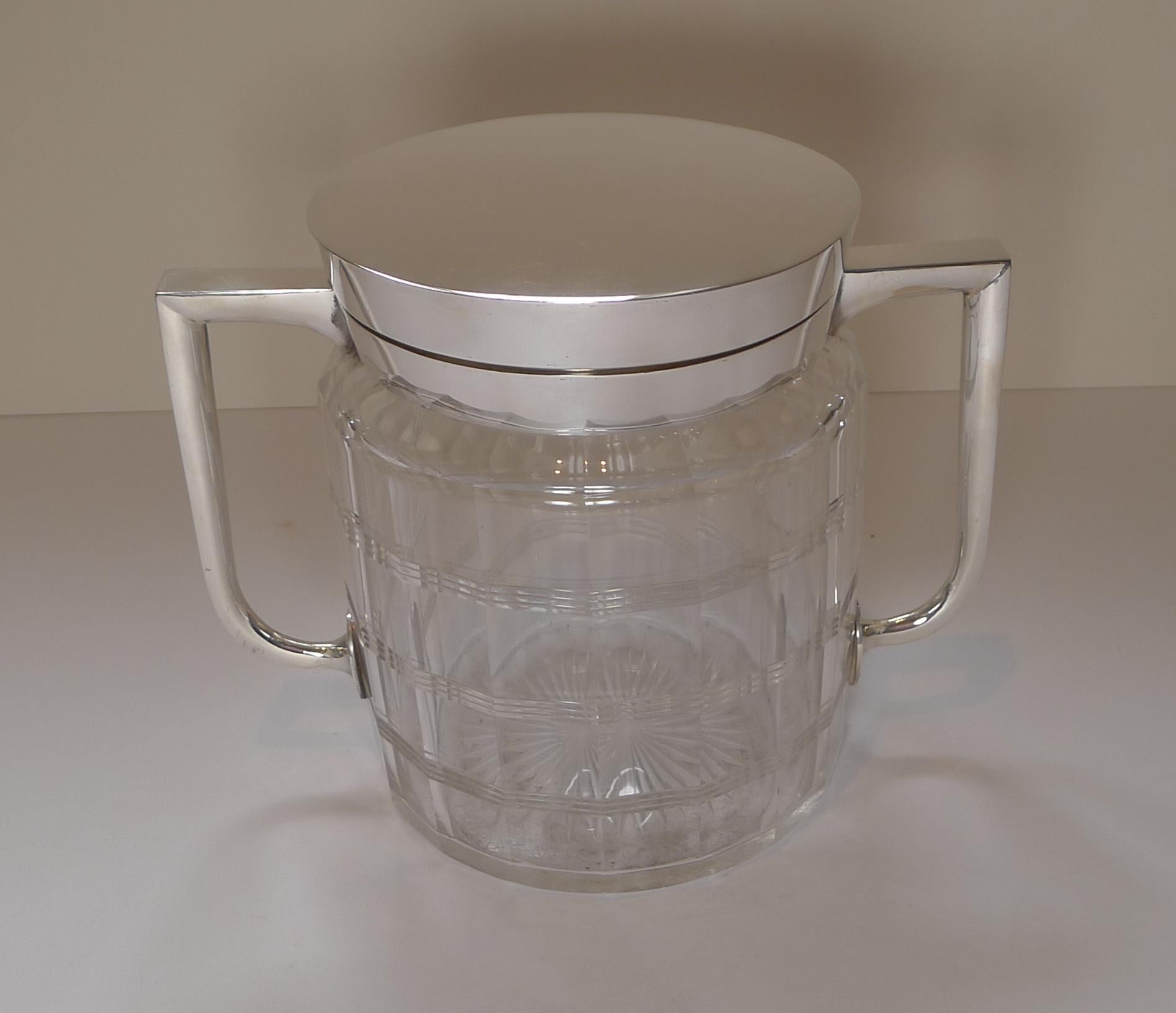 A heavy piece of glass was used to create this quality example, faceted all the way around and series of simple linear cuts around the circumference; the underside having a star cut. 

The striking Art Deco handles and the hinged lid are silver