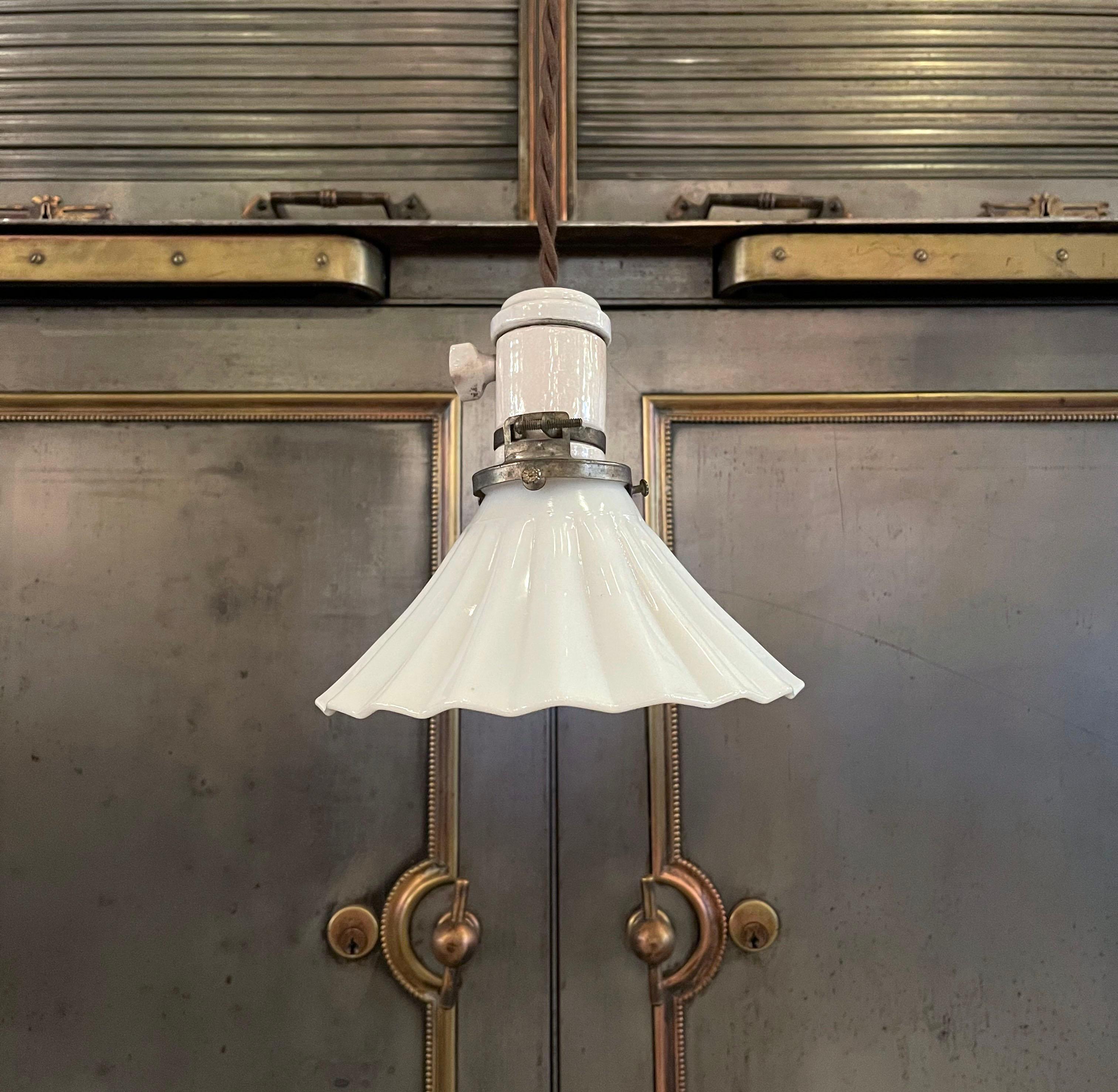 Petite, early 20th century pendant light with fluted milk glass shade and porcelain socket and canopy is newly wired with brown braided cloth cord to hang at an overall length of 33.5 inches. The canopy backplate measures 3.5 inches diameter.