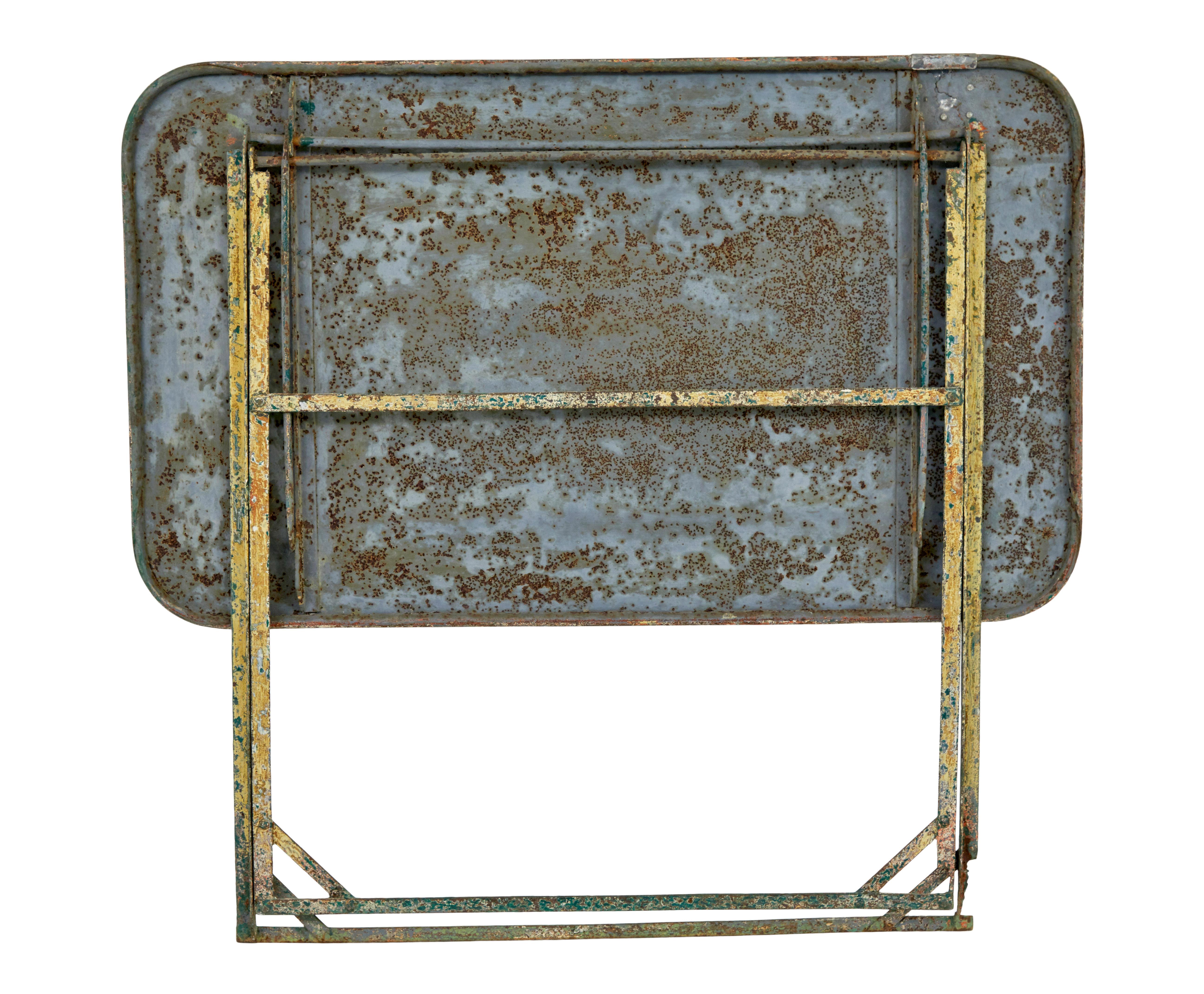 Tavolo da giardino pieghevole dei primi del Novecento, circa 1920.

Tavolo da giardino in acciaio, piano rettangolare con bordi arrotondati, gambe con struttura tubolare.  Almeno 3 o 4 strati di vernice sulla superficie superiore che si sta