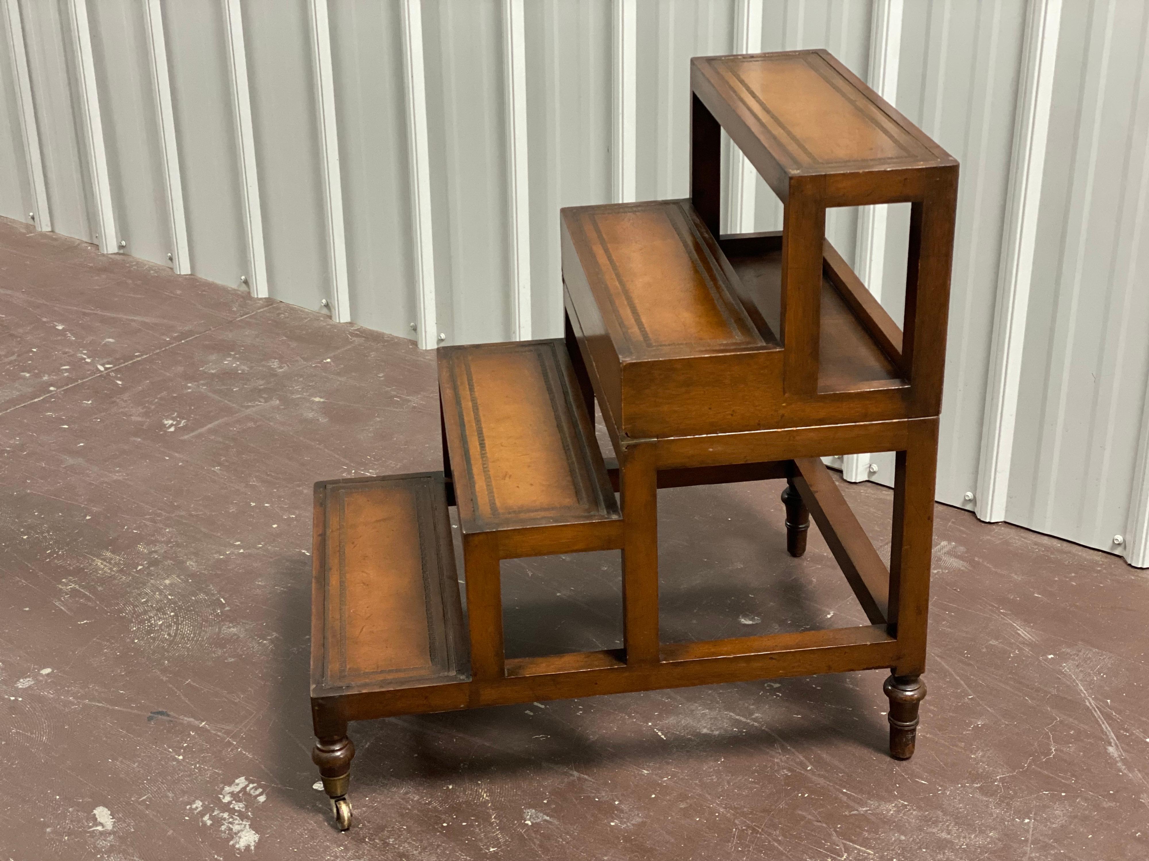 Early 20th century folding library steps/table. Mahogany Library steps with inset tooled leather surfaces. Stains to leather, repaired splits to one leg, wear from use. Featuring four steps when opened. Closes to a leather top coffee table. Two legs