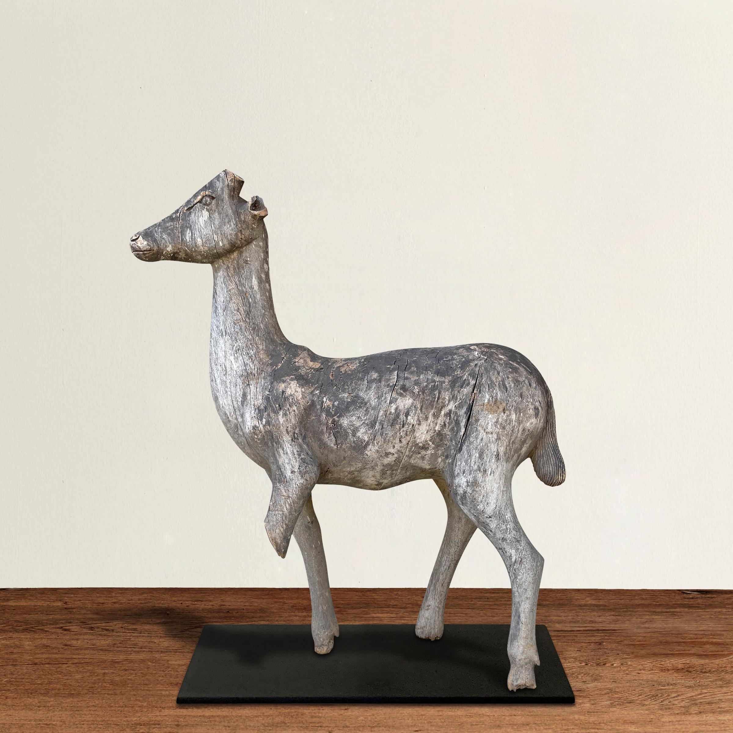 A stoic yet charming early 20th century Folk Art carved wood deer sculpture, nearly life size, with a wonderful dry weathered finish, and mounted on a custom steel mount. Perfect displayed on the floor, but we think it would be striking on top of a