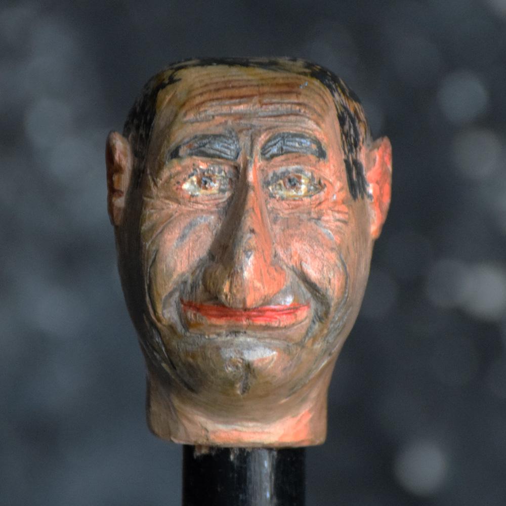 Un esempio insolito e molto caratteristico di bastone da passeggio per gentiluomini inglesi dell'inizio del XX secolo, con punta in ottone, fusto ebanizzato e una testa d'uomo comica tipica della Folk Art sulla mano. Tutto è scolpito nel legno e la