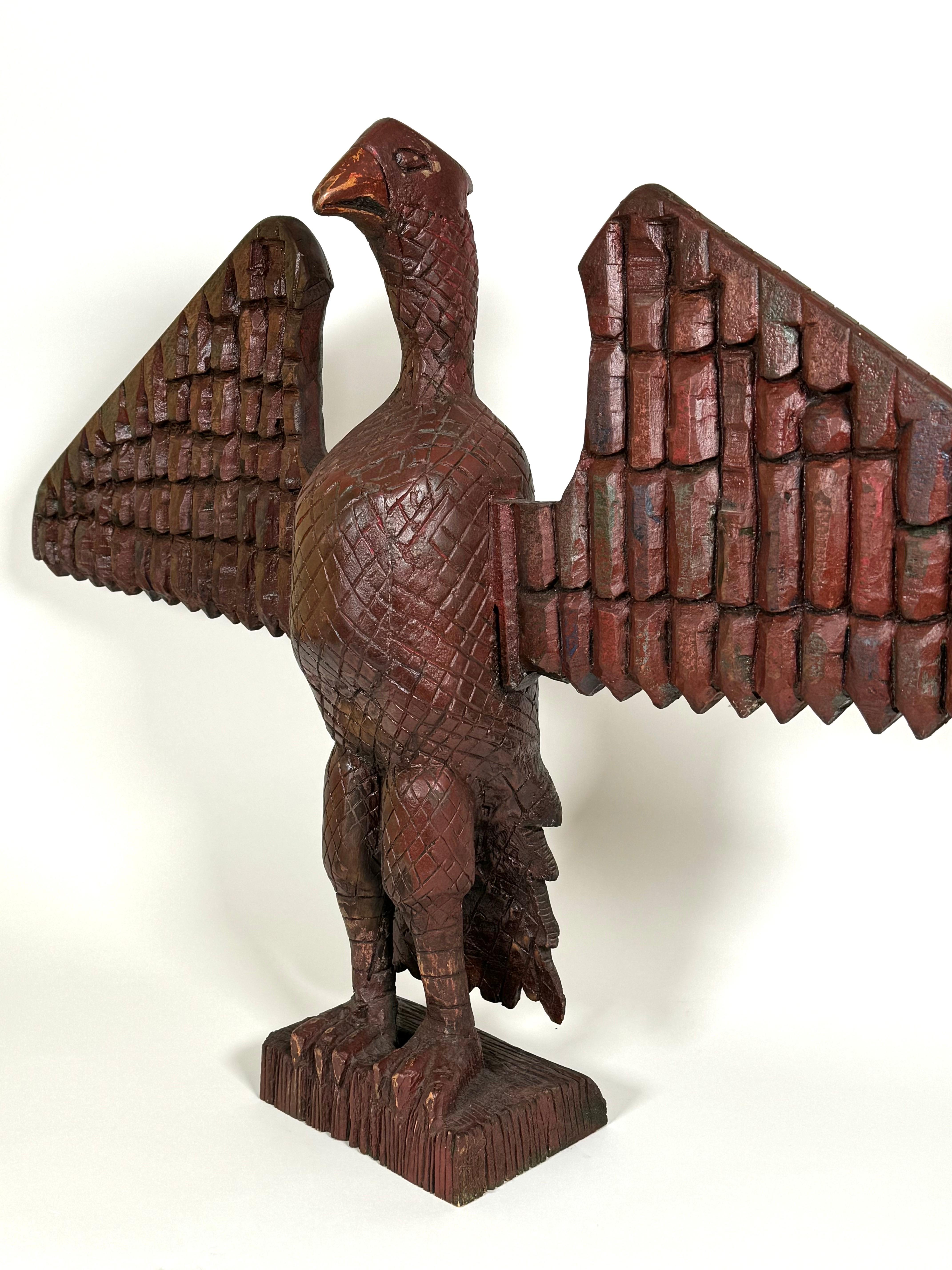 Early 20th Century hand carved wooden eagle with a red wash finish.  The eagle has out stretched wings and a up right posture resting on a rectangular wooden base. Extensive carving details on the entire sculpture reminiscent of the work of American