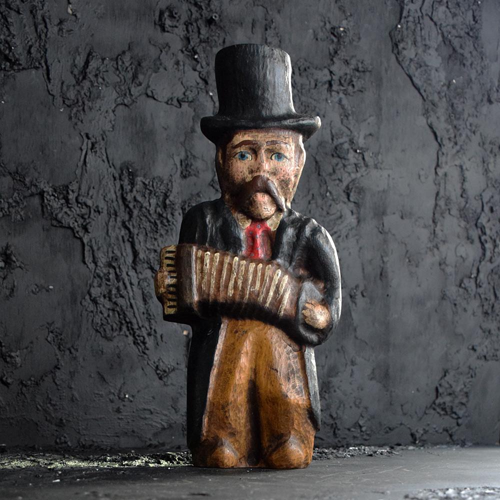 Figura di musicista di arte popolare dell'inizio del XX secolo.

Una figura in legno di quercia intagliata di arte popolare inglese dei primi del Novecento raffigurante un musicista che suona una concertina. Pittura policroma con dettagli naif.