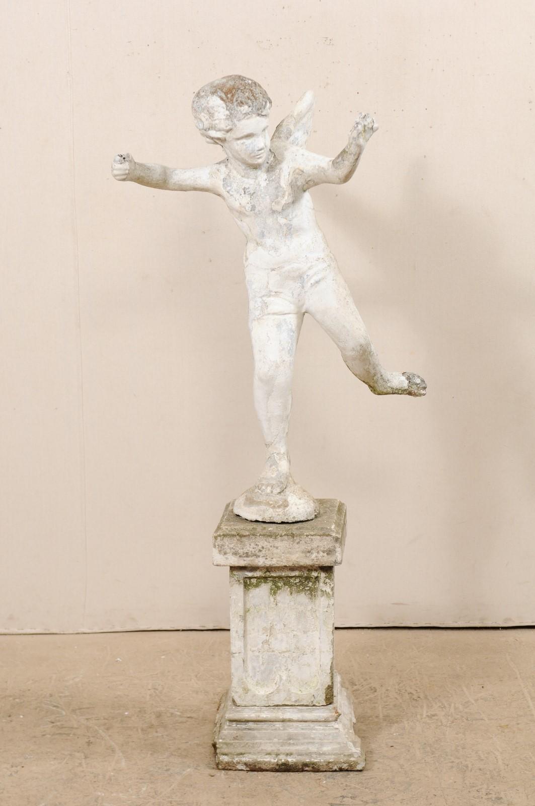 A tall French garden sculpture of a winged boy angel from the early 20th century. This antique statue from France sweetly depicts the figure of Cupid with arms raised as if he would be shooting an arrow, and one leg raised. The statue is presented