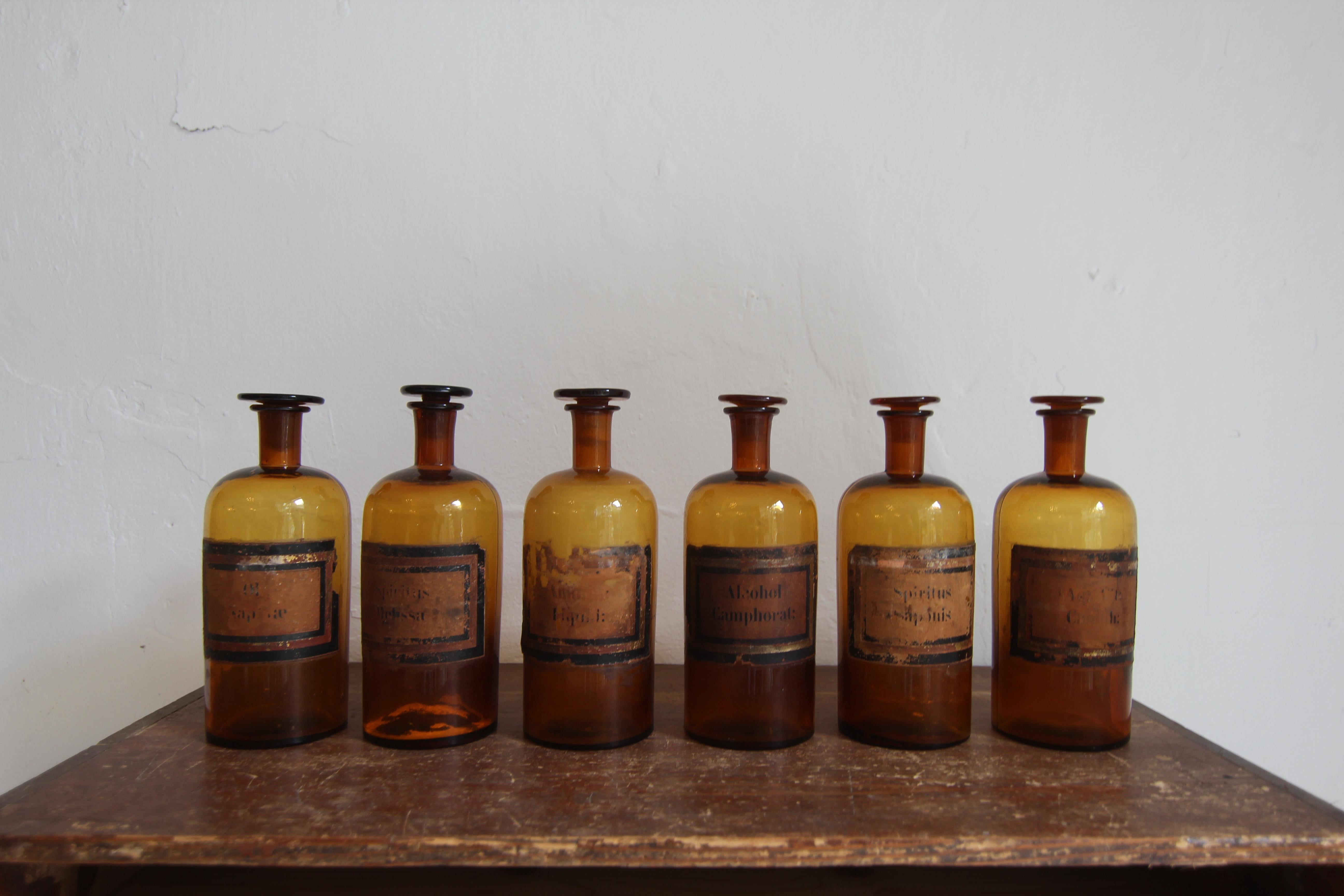 Un ensemble très décoratif de six pots d'apothicaire en verre français du début du 20e siècle. 
Les bouteilles en verre ambré opaque, dessinées à la main, sont munies d'un bouchon en verre taillé et possèdent encore l'étiquette d'origine. 