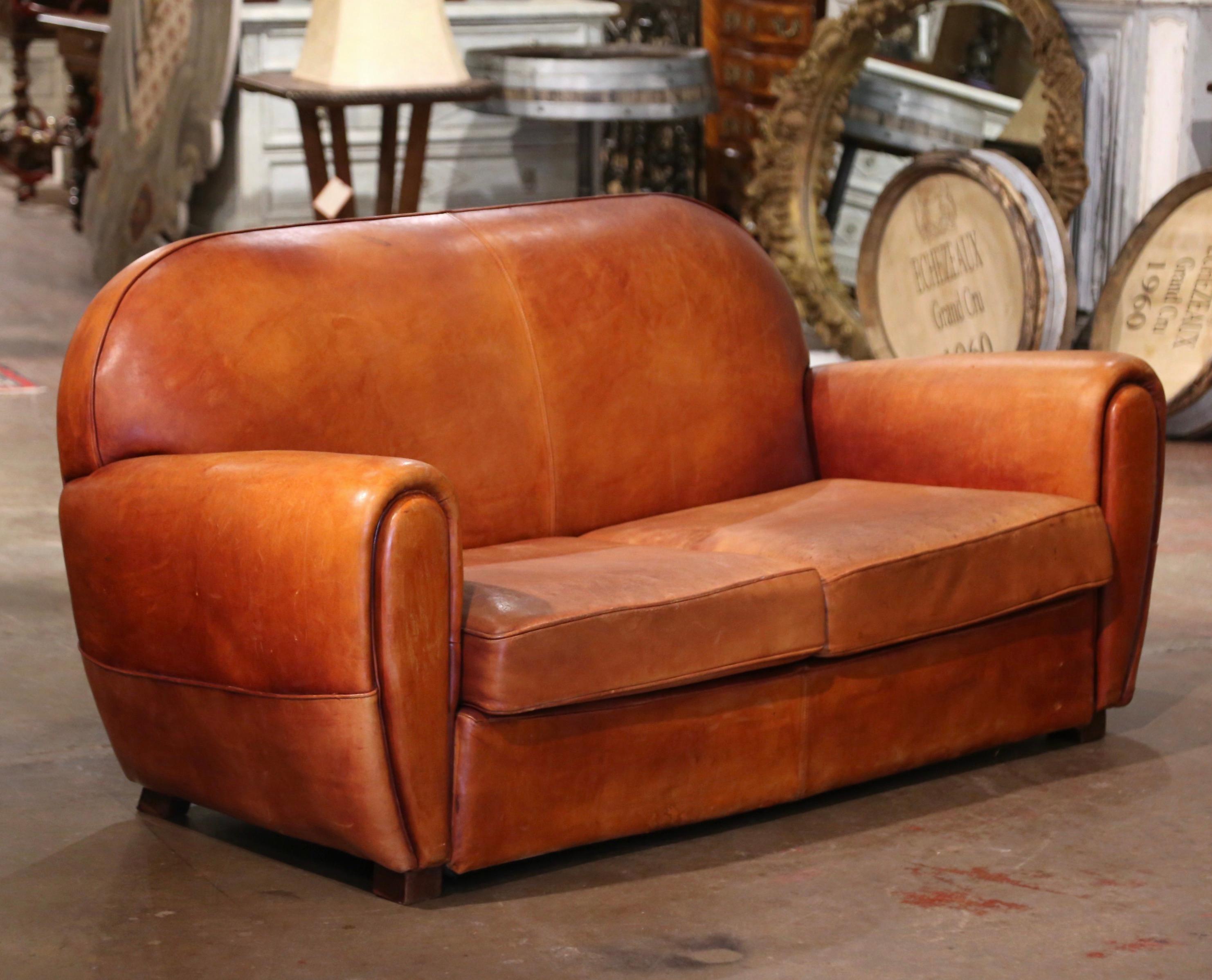 This Classic, antique Art Deco club sofa was crafted in France, circa 1920. This stately couch features wide, rounded armrests, a pitch back with an arched top shape, and square feet covered with leather at the base. The Classic, masculine French