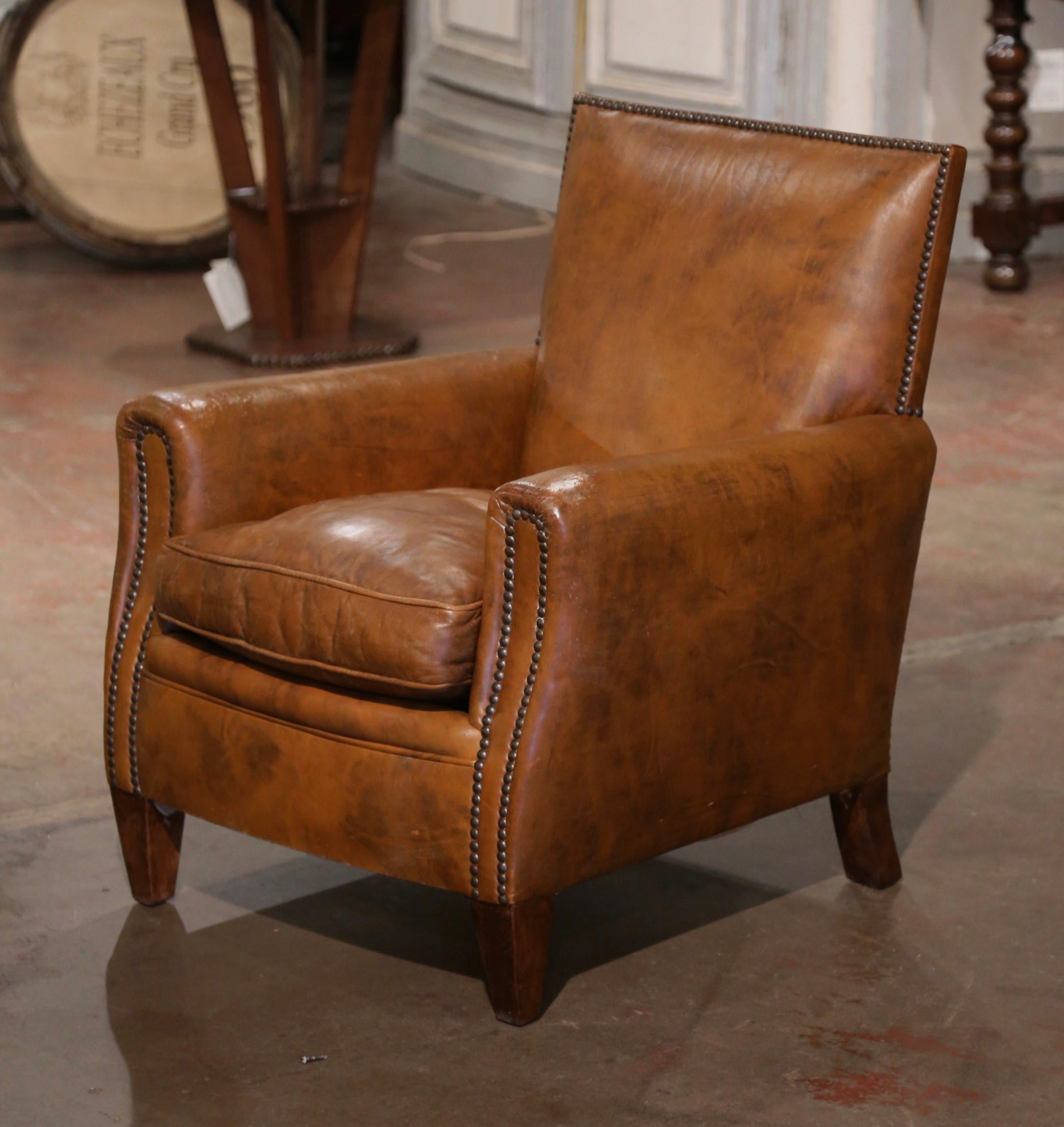This Classic, antique Art Deco club chair was crafted in France, circa 1320. The stately chair stands on tapered wooden feet and features wide, rounded armrests, a pitch back with a flat top shape, and a deep loose seat cushion. The Classic,