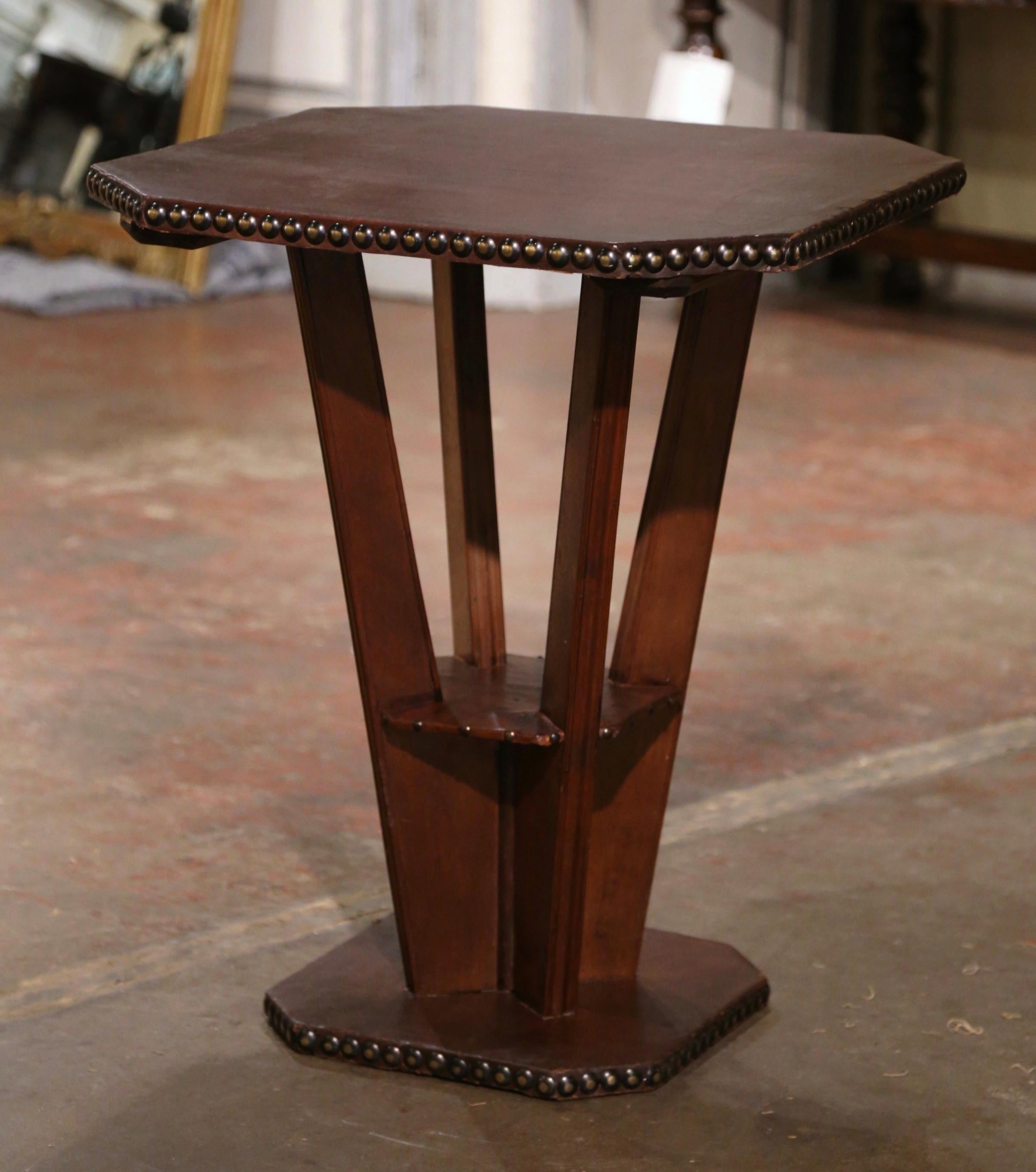 Decorate a den or an office with this elegant antique side table. Crafted in France circa 1930 and square in shape with cut corners, the gueridon stands on a flat hexagonal base over four post legs. The table is upholstered with a patinated brown