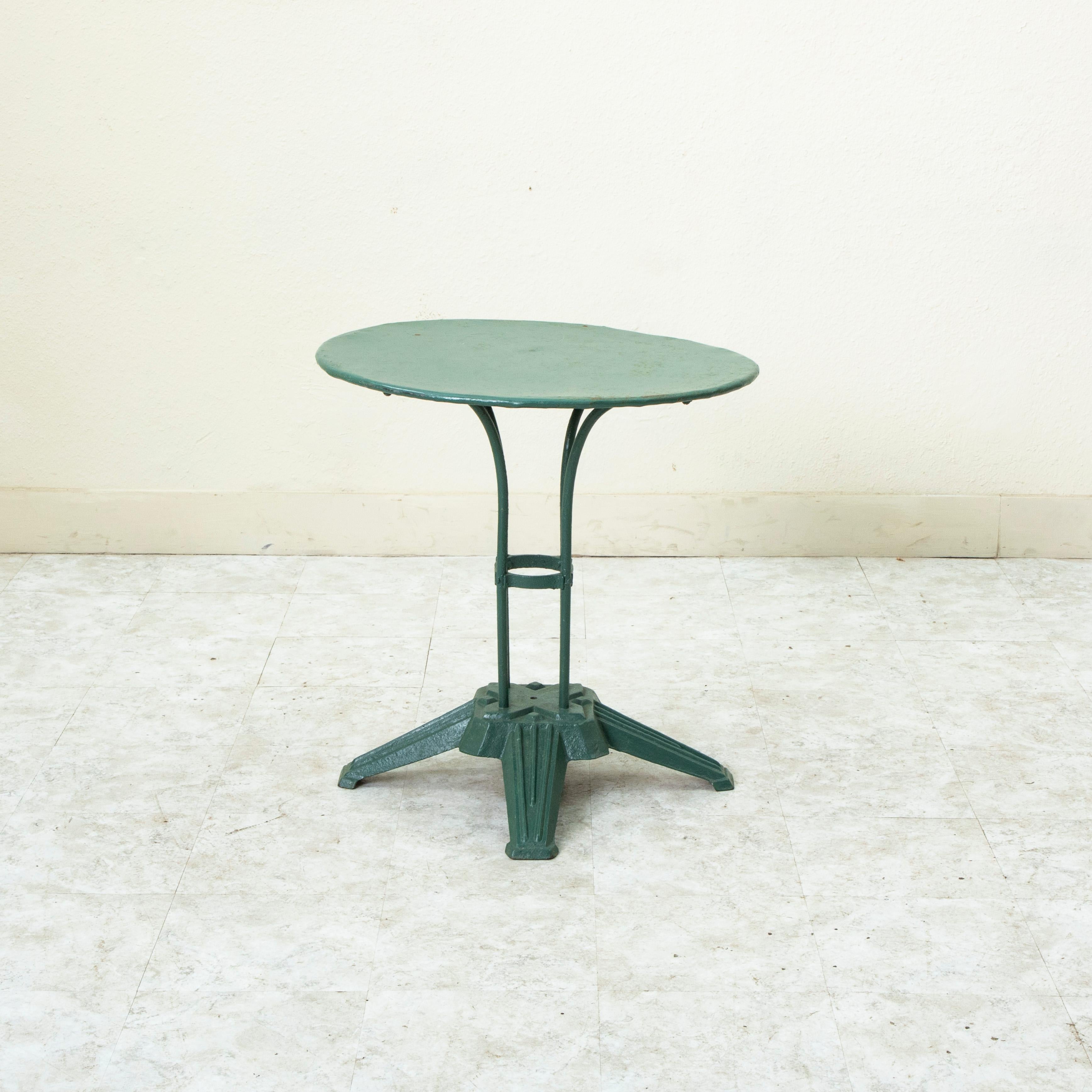 This early twentieth century French Art Deco period round garden table features a metal top on a cast iron pedestal base. The green painted base is made up of four iron legs that rest on a square base. The legs are joined by a central circlet. The