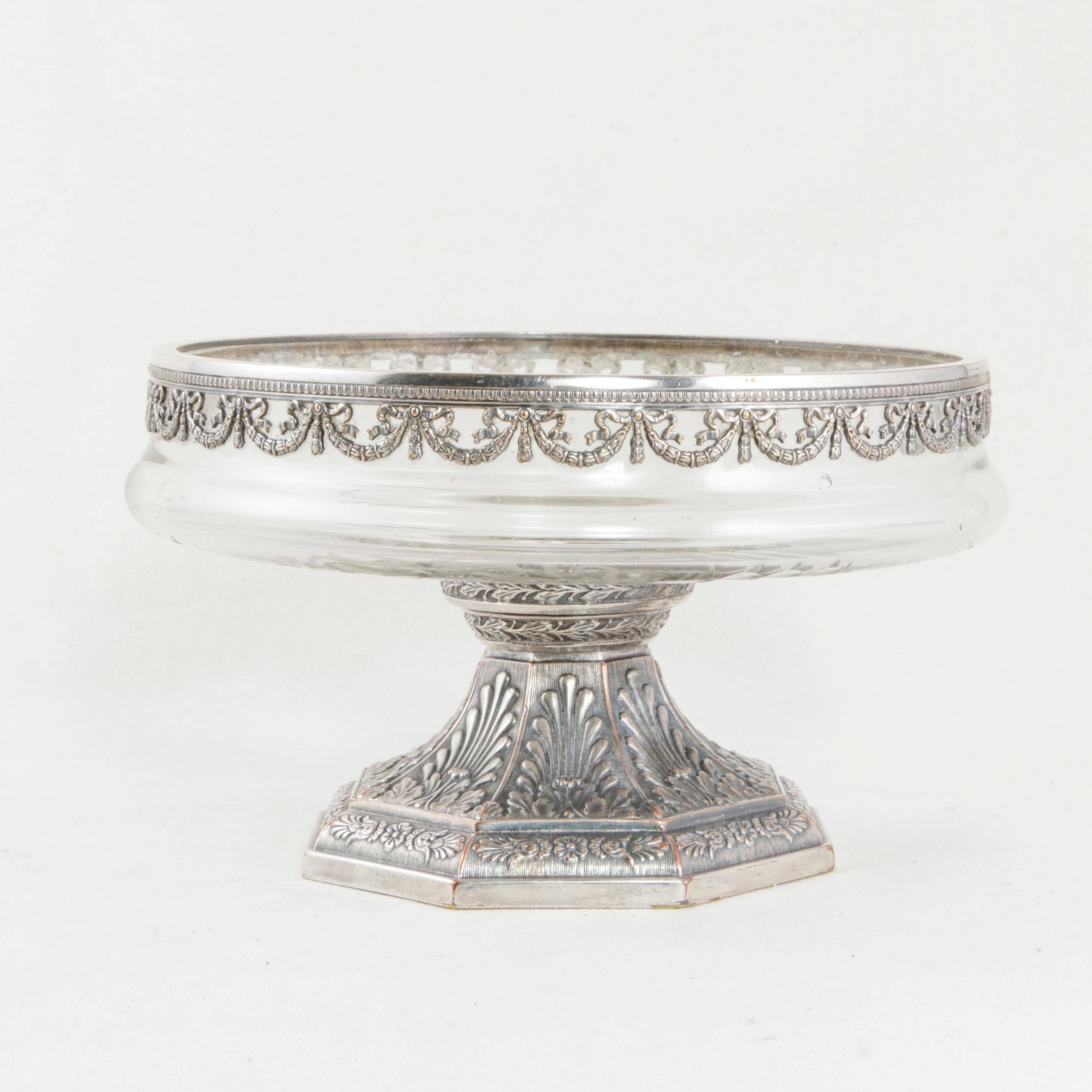 This early 20th century French Art Deco period etched crystal compote or serving dish features a silver plate footed base and rim displaying Classic Louis XVI motifs. The crystal bowl is detailed with etched knotted ribbons and flowers. A beaded