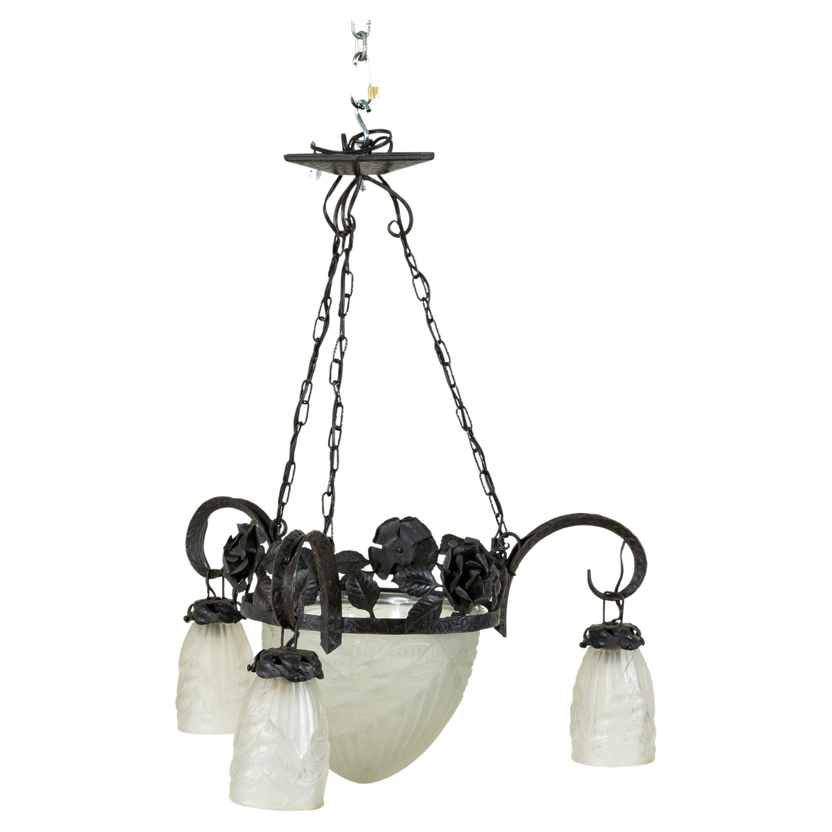A blend of Art Deco and Art Nouveau, this early twentieth century French iron and glass chandelier features a central wreath of iron roses and leaves suspended from three chains joined to the ceiling mount. A central frosted glass globe finished