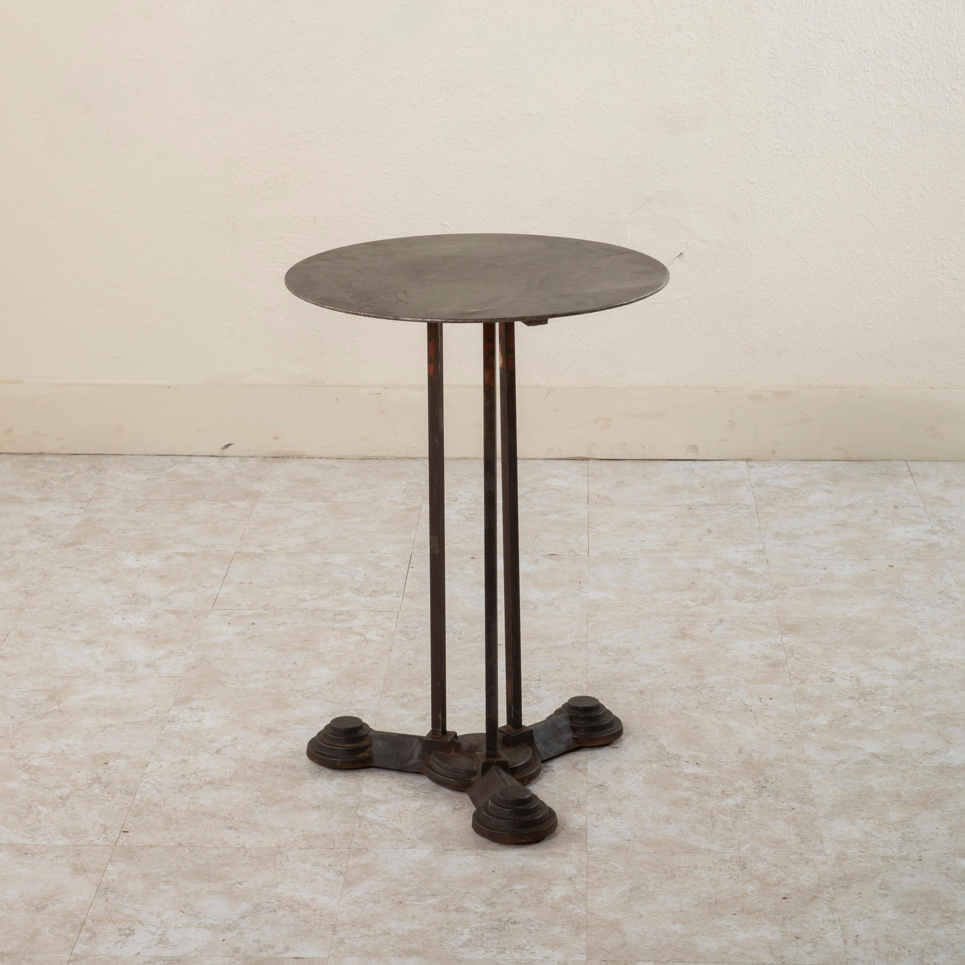 This early twentieth century French Art Deco period iron bistro table or side table features a 20 inch diameter metal top. The top rests on three legs joined to a tripod base. The feet of the base are detailed with concentric terraced circles