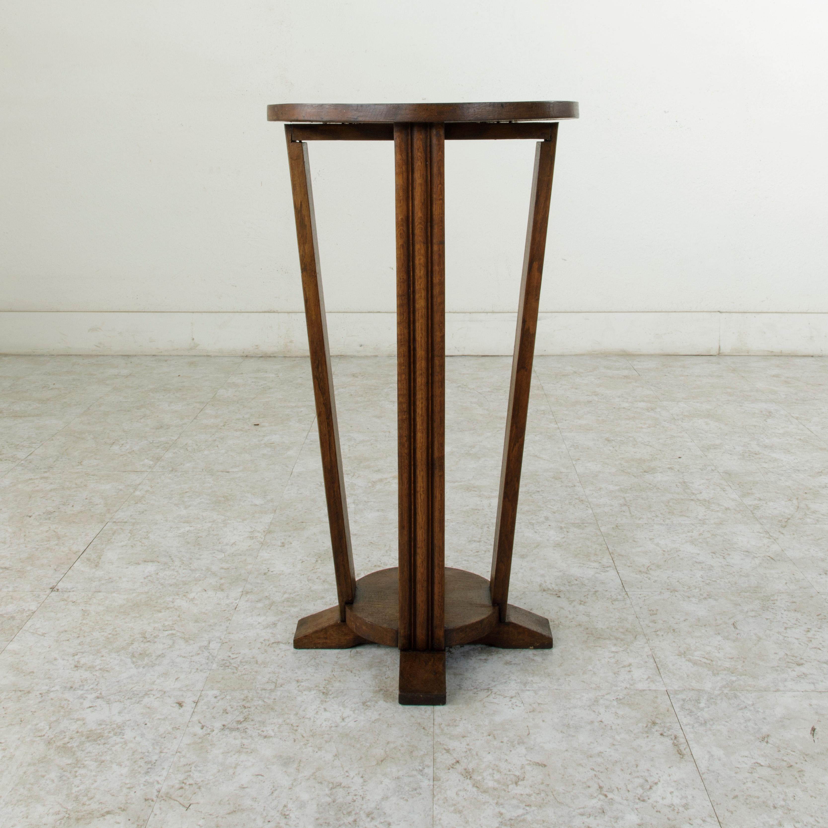 This early twentieth century French Art Deco period pedestal or side table is constructed of solid oak and features a 17 inch diameter top. The top is supported by four fluted legs that join a lower base. Its lower level provides additional display