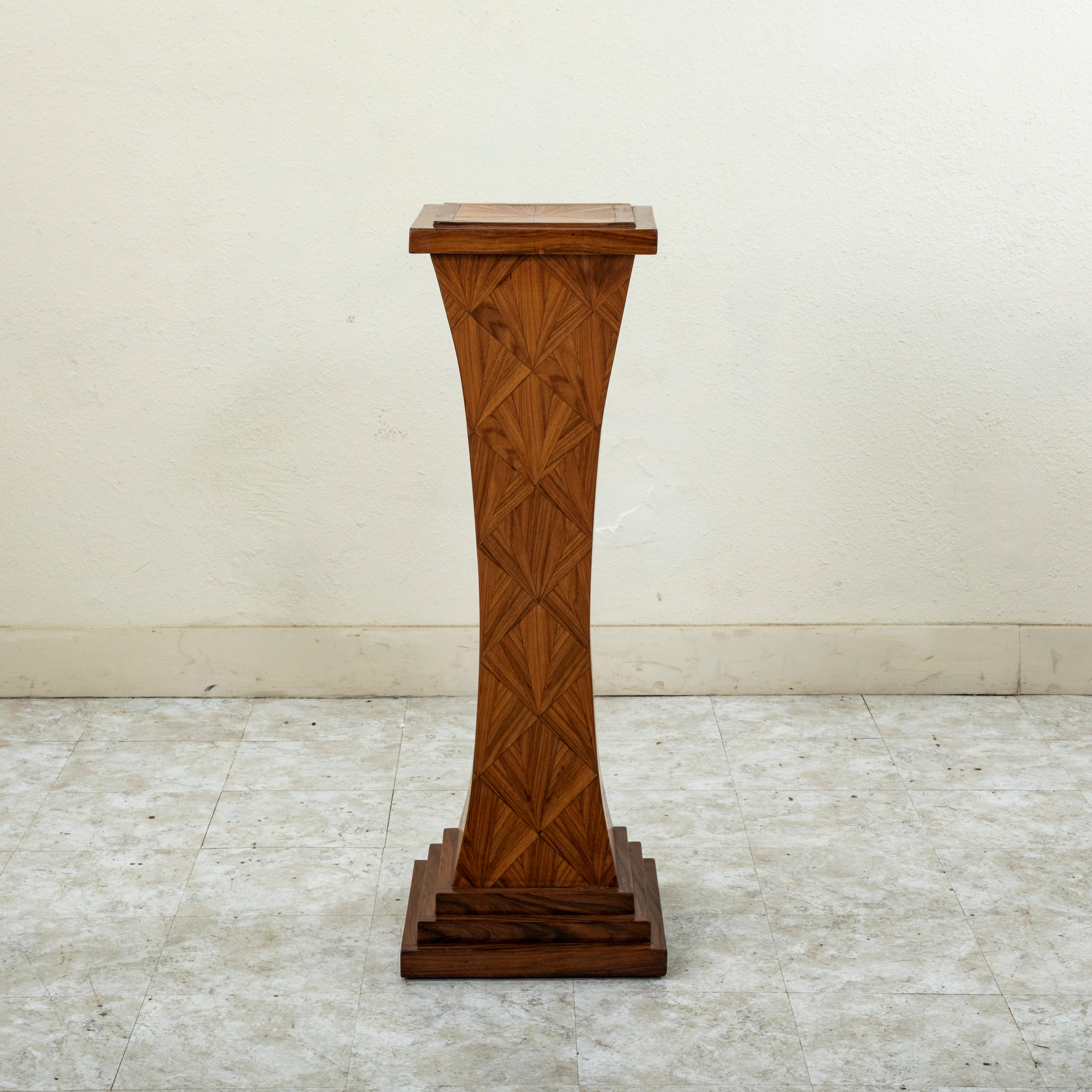 This early twentieth century French Art Deco period sculpture stand or pedestal features a rosewood and palisander marquetry facade with sides that curve inward detailed with a geometric fan pattern. Its 13.5 inch square top is inlaid with a