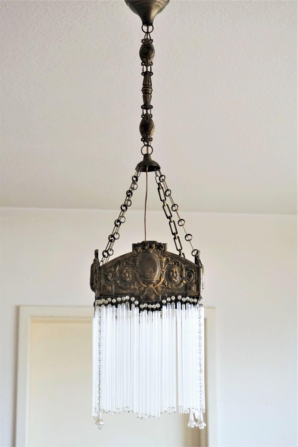 A lovely Art Nouveau chandelier, France, circa 1900-1910. Brass body decorated with handcrafted high relief details, long glass rods and glass pearls.
Very good condition, brass with beautiful patina, rods are complete.
Fully functional: European