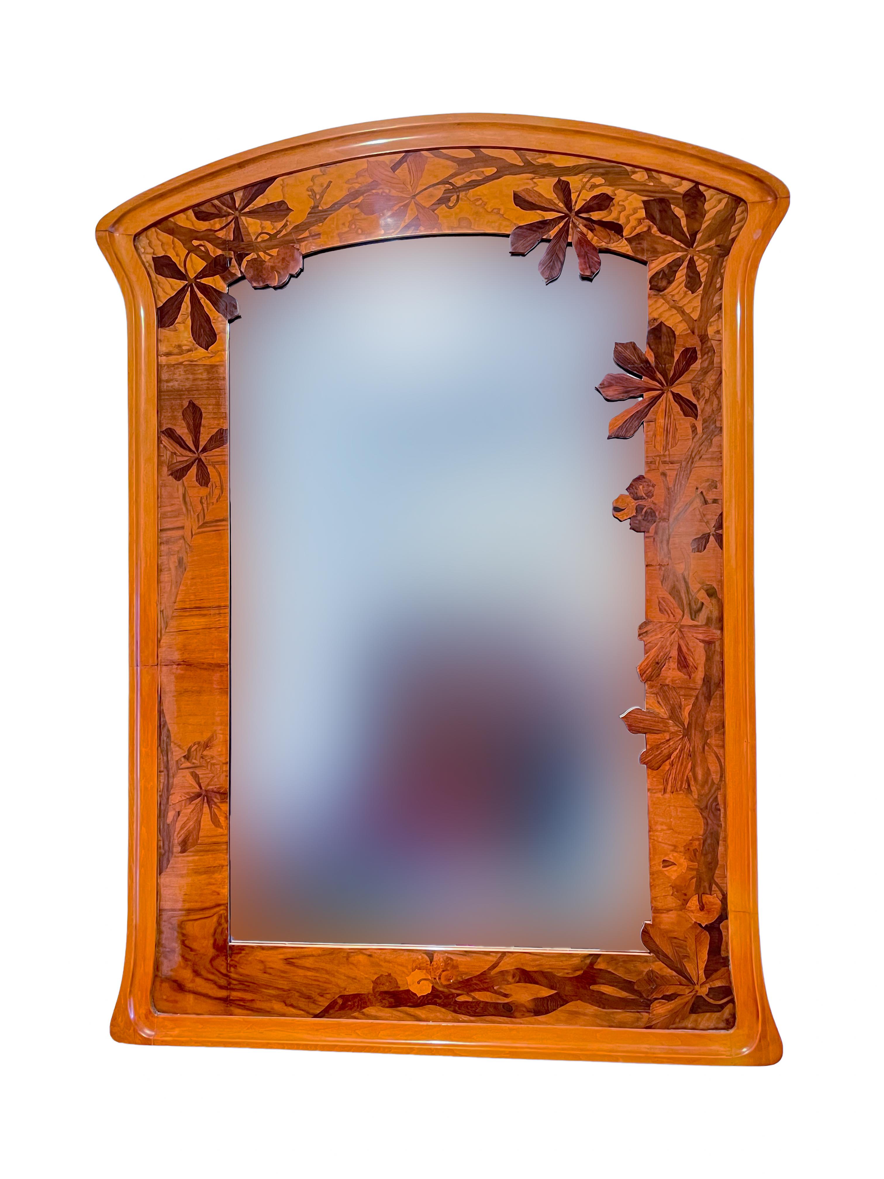 An impressive early 20th century French Art Nouveau marquetry and carved wood wall mirror by, Louis Majorelle with various wood inlay marquetry decoration of maple leafs throughout all inlaid into a solid carved wood frame with its beveled glass