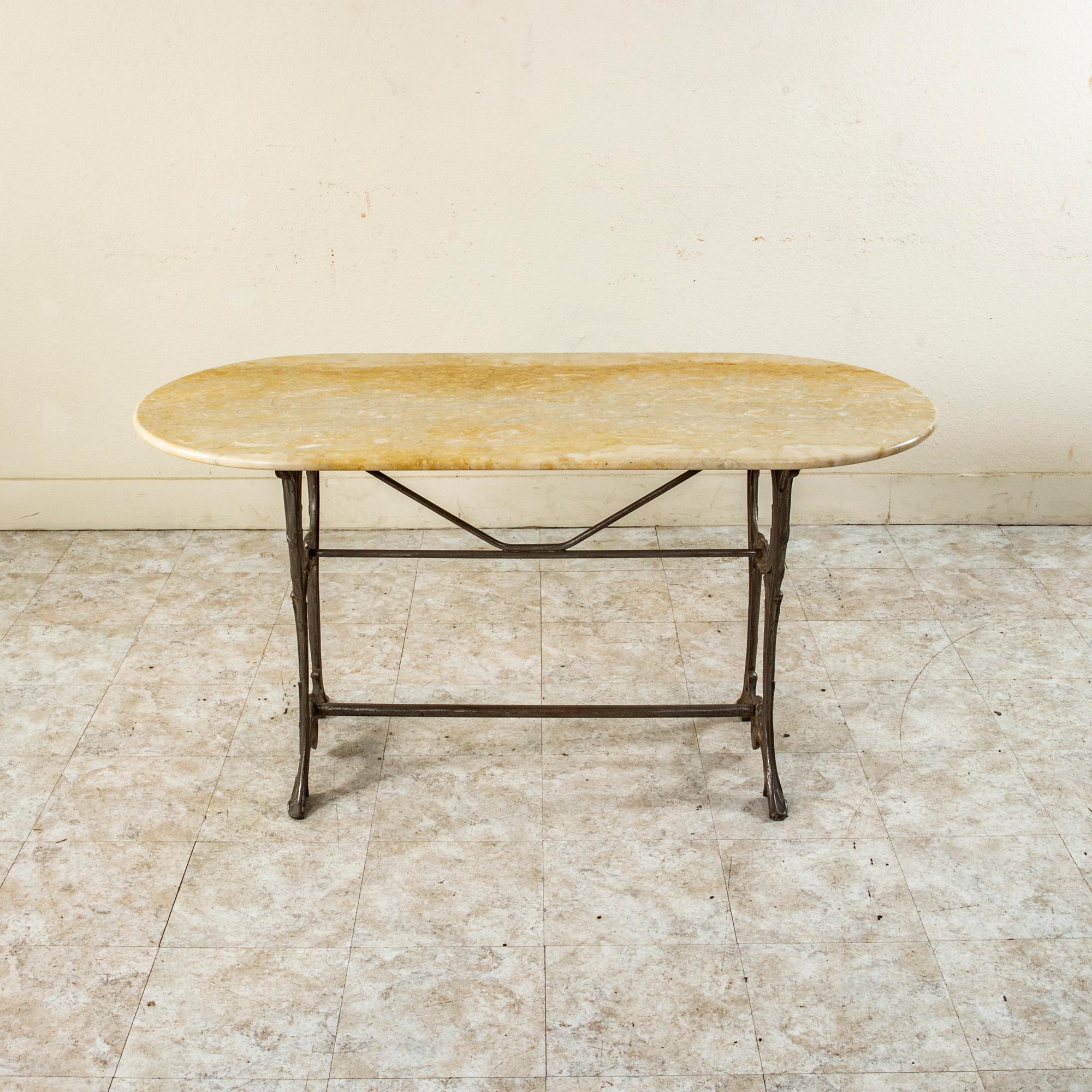 This French Art Nouveau Period iron bistro table from the turn of the twentieth century features an oval marble top. The base of the table is detailed with classic Art Nouveau scrolling leaves and shells. The legs are joined by two stretchers. The