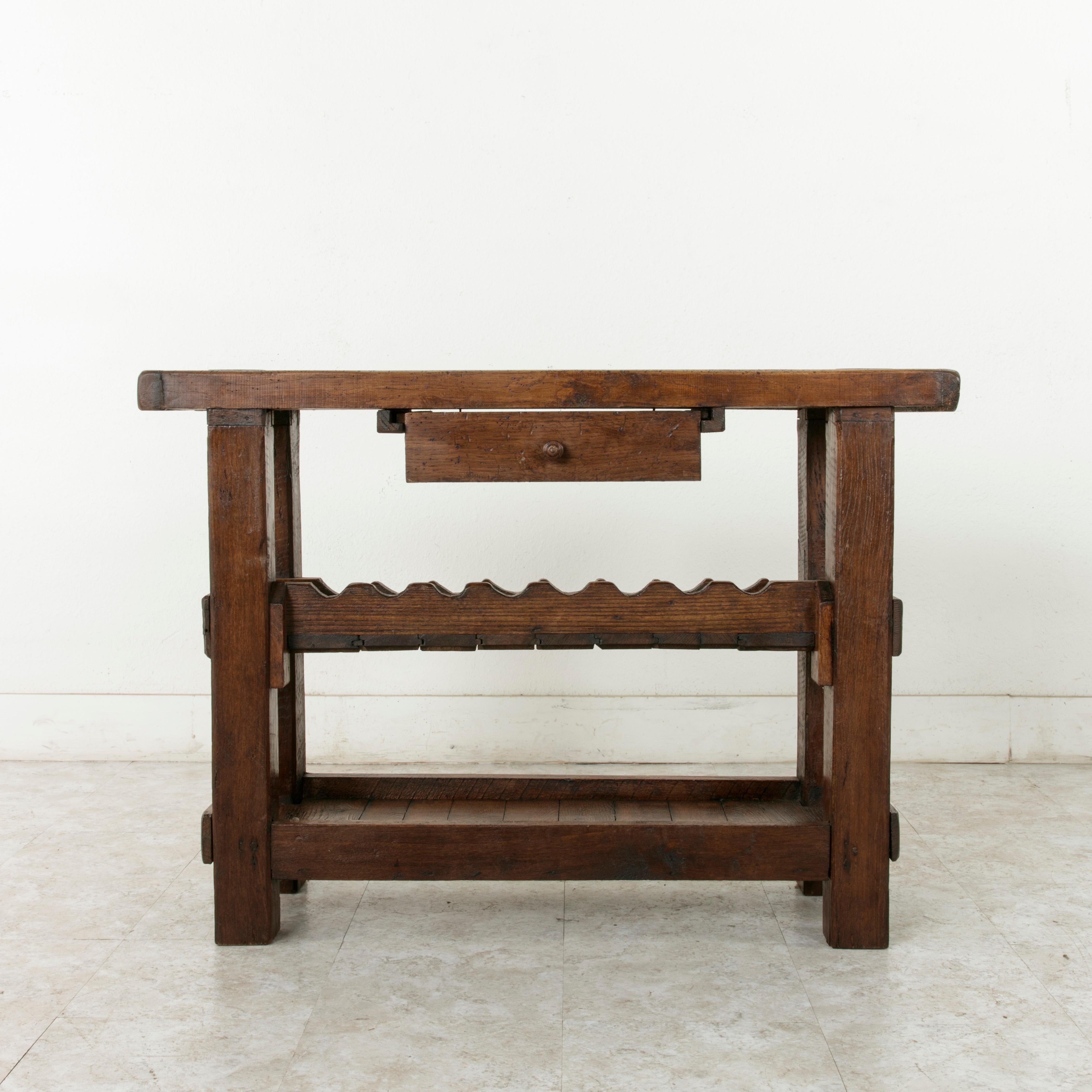 This early 20th century French oak workbench from Normandy, France, features the engraved name of the original owner, M. Mauduit, in the lower left corner of its two inch thick top. Two slots at the back of the top once kept the artisan's tools