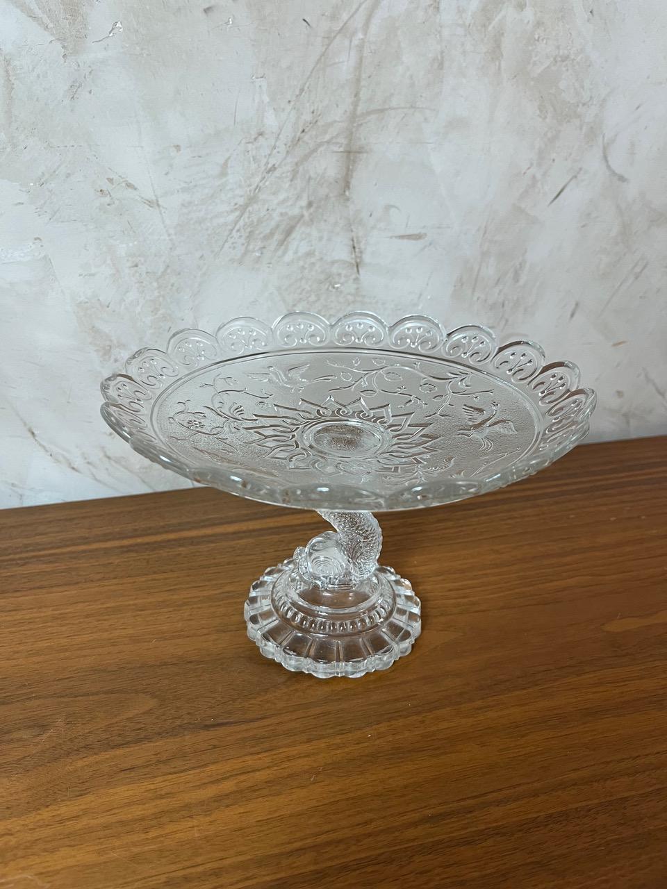 Compote en verre à pied dans le style de Baccarat, présentant d'élégants motifs floraux et des décorations finement détaillées. Cette pièce vintage, en verre pressé, est parfaite pour servir des fruits, des gâteaux, ou simplement comme accent