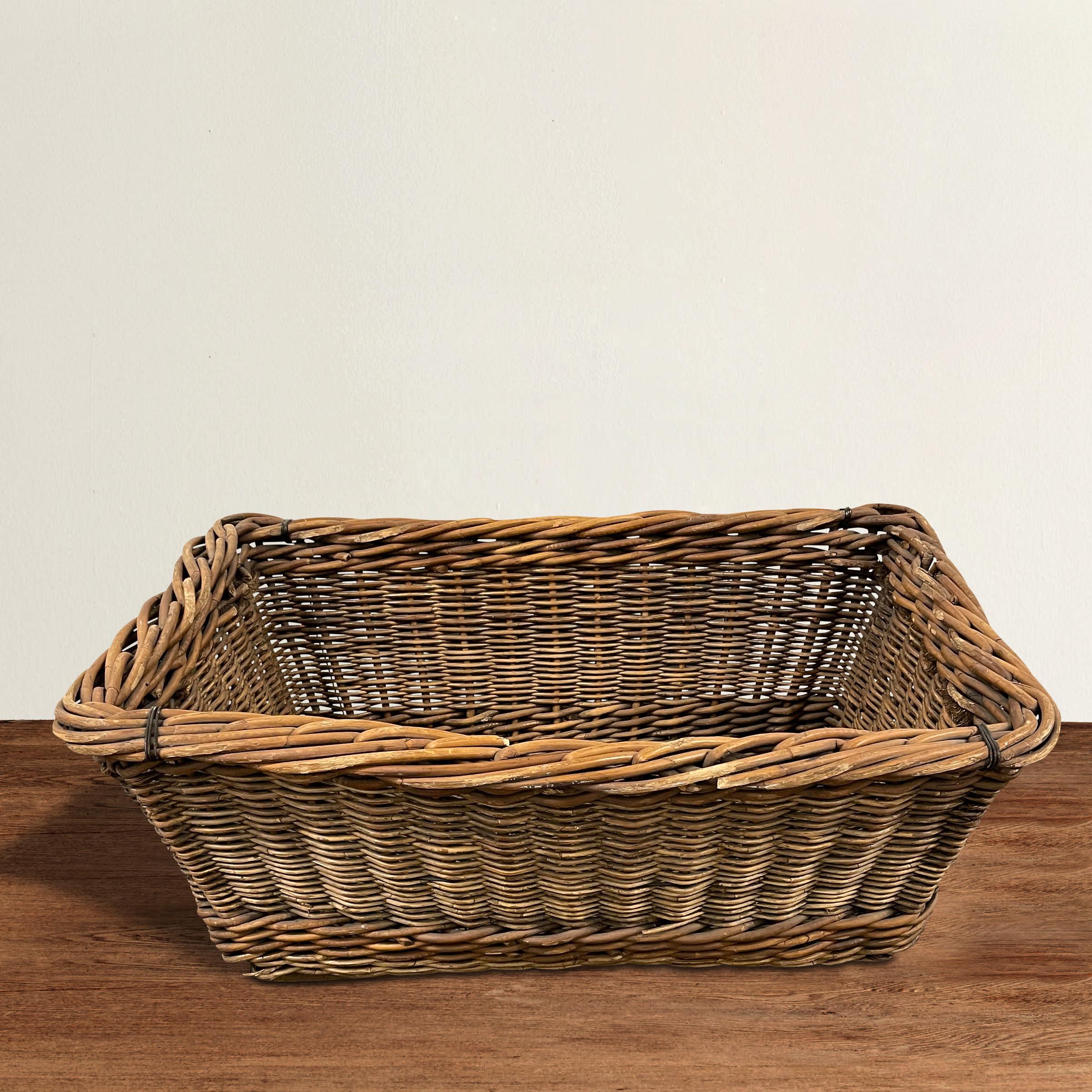 A charming early 20th century French vineyard basket hand-woven from reeds with a heavy rim, rope handles, and wooden slat bottom. Perfect for laundry, or filled with throw pillows and blankets in your family room.