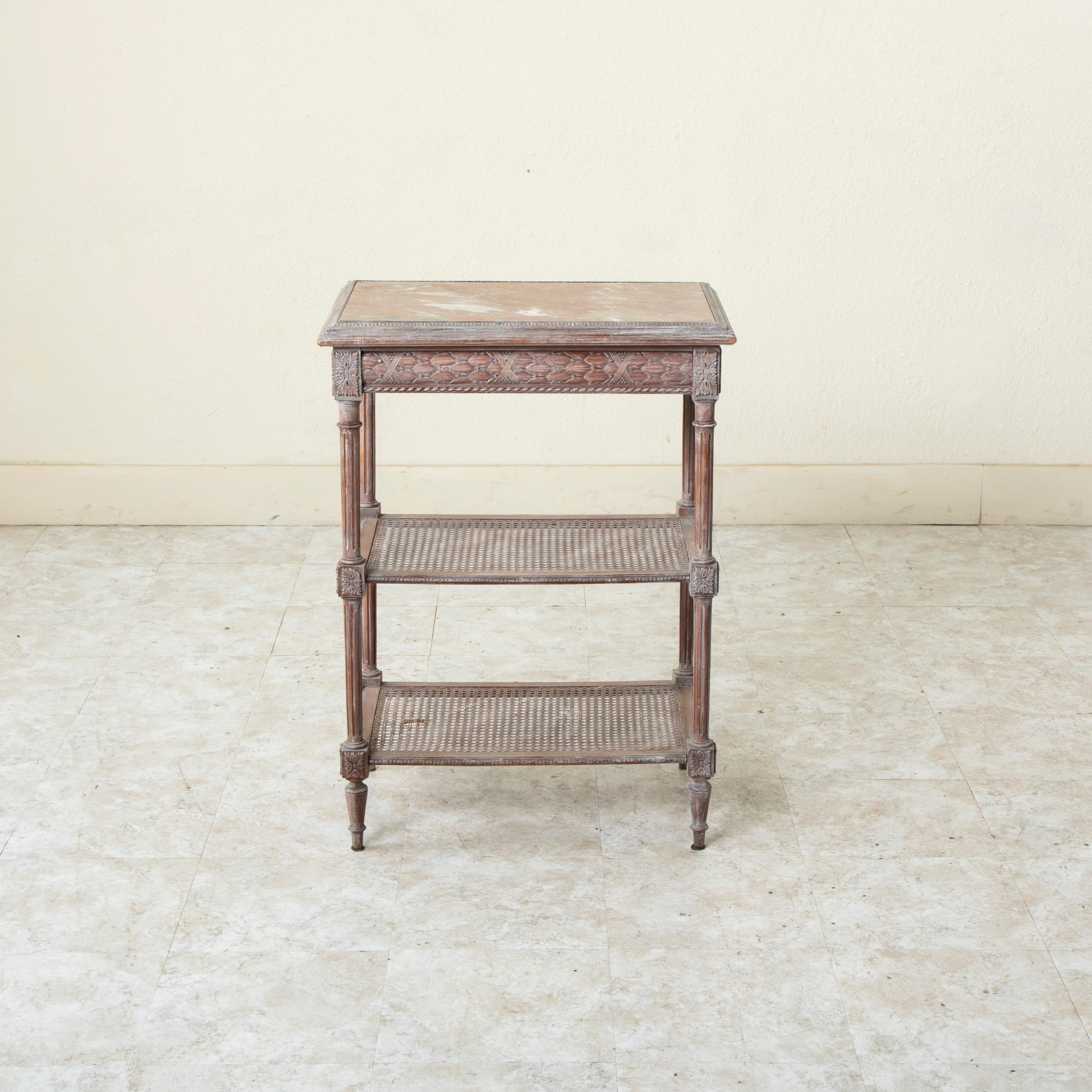 Cette petite table d'appoint en bois de hêtre sculpté à la main de style Louis XVI français du début du XXe siècle présente un plateau en marbre de couleur rose avec des veines grises et blanches. Un motif de rais-de-coeur entoure le marbre et des