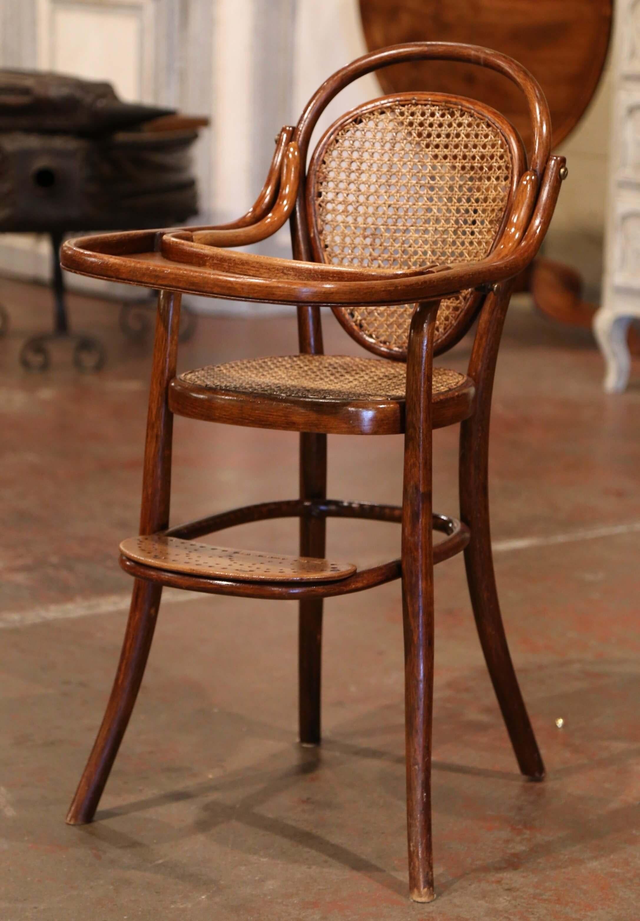 Feed your child in style in the antique and sturdy Art Deco high chair; crafted in France of bentwood circa 1920 attributed to Michael Thonet (1796-1871), the child chair stands on four curved legs embellished with a pierced footrest on the front;