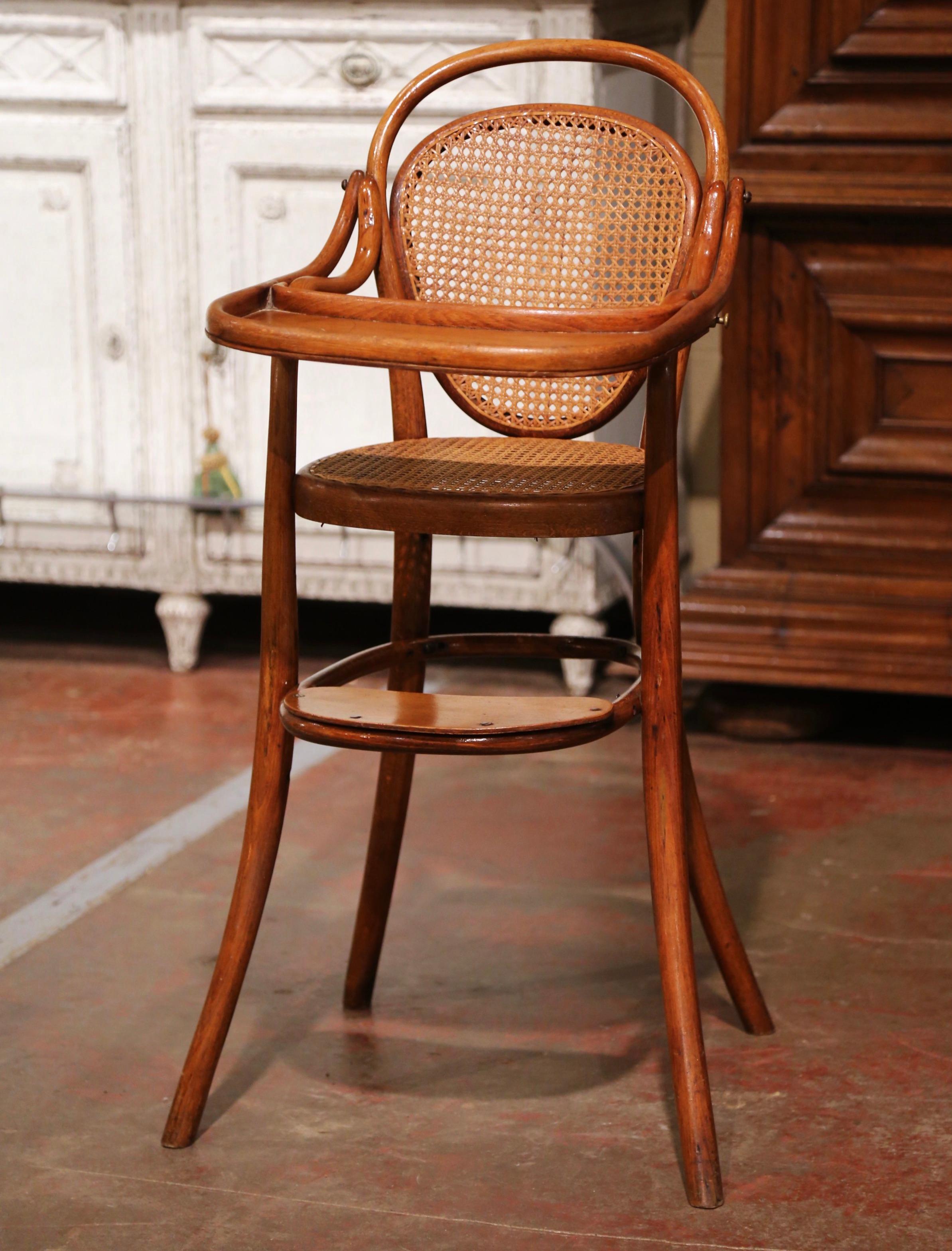 Feed your child in style in the antique and sturdy Art Deco high chair; crafted in France of bentwood circa 1920, and attributed to Michael Thonet (1796-1871), the child chair stands on four curved legs over a footrest on the front; both seat and