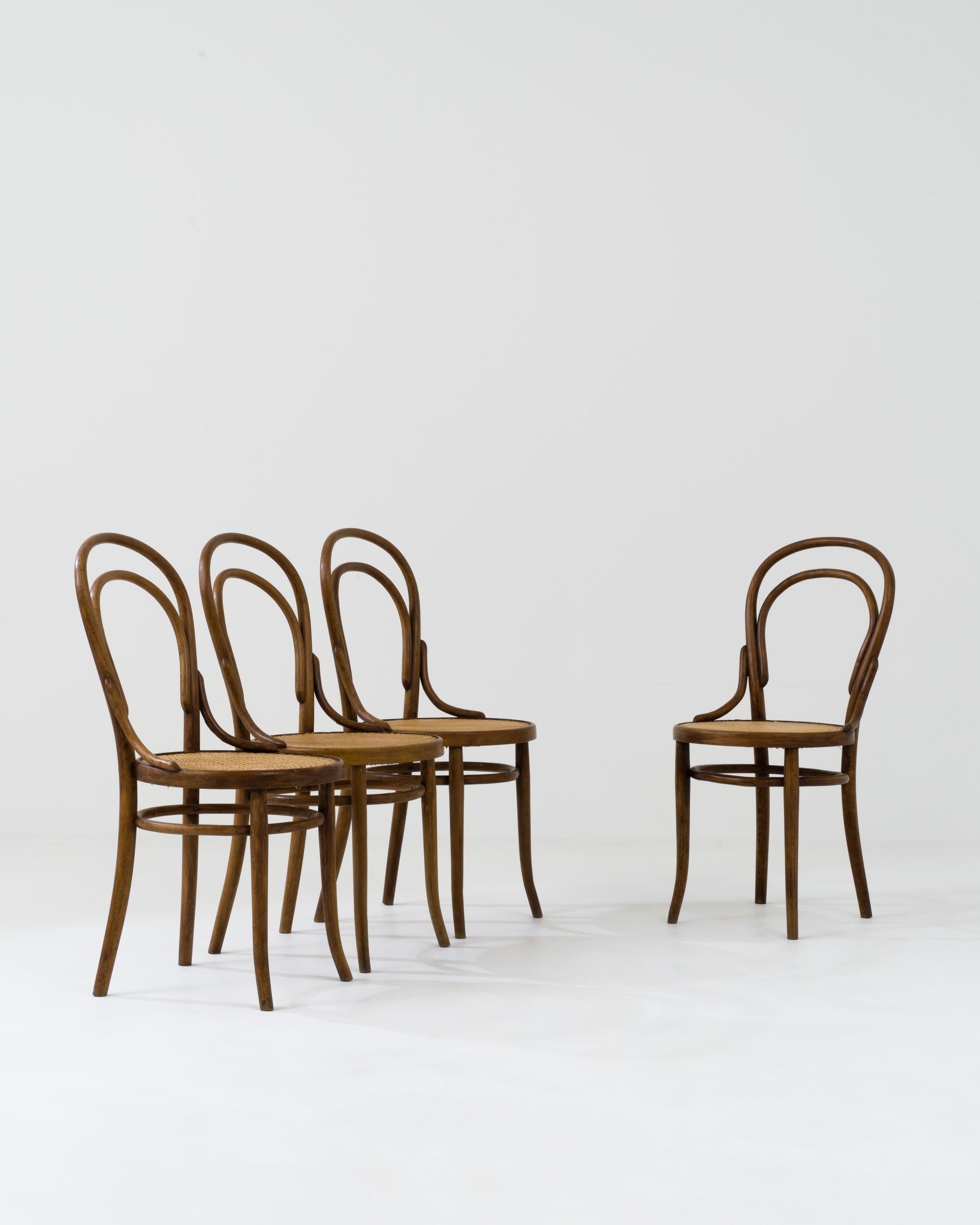 This set of early 20th-century dining chairs was crafted in France. The rounded sculptural backrests seamlessly transition into the back legs, which are supported by elegant circular side stretchers, creating an alluring geometric interplay. The