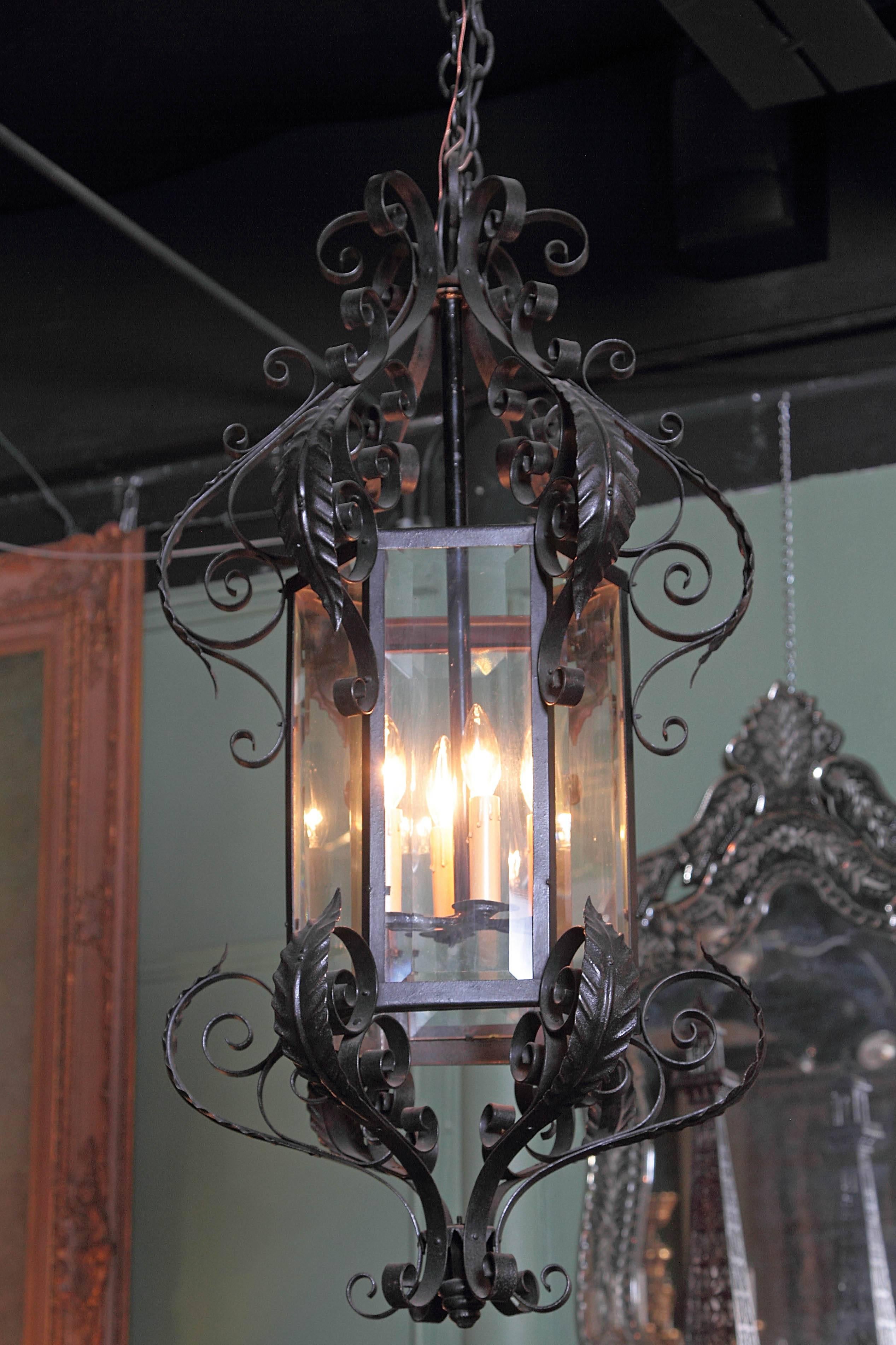 This elegant, hexagonal iron lantern was created in France, circa 1900; with six sides, beveled glass panels, and an ornate scroll iron frame with leaf decor on top and bottom, the tall light fixture truly stands out and would make a wonderful