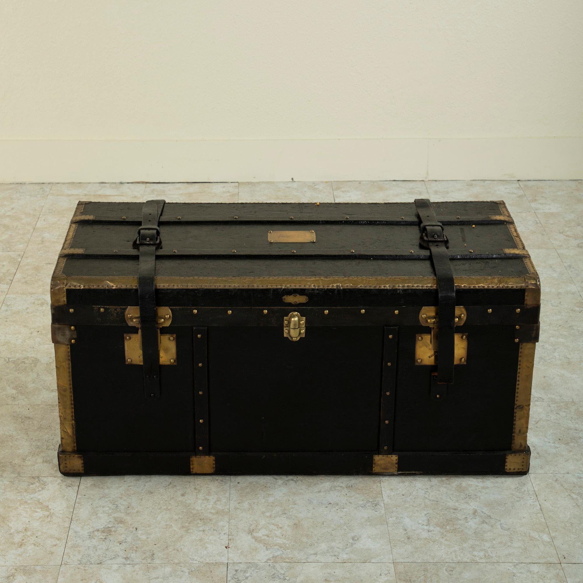This French wooden steam trunk from the turn of the 20th century is covered in black leather and features wooden runners and brass corners that offered protection from damage when traveling. Its original leather handles and straps are still intact.