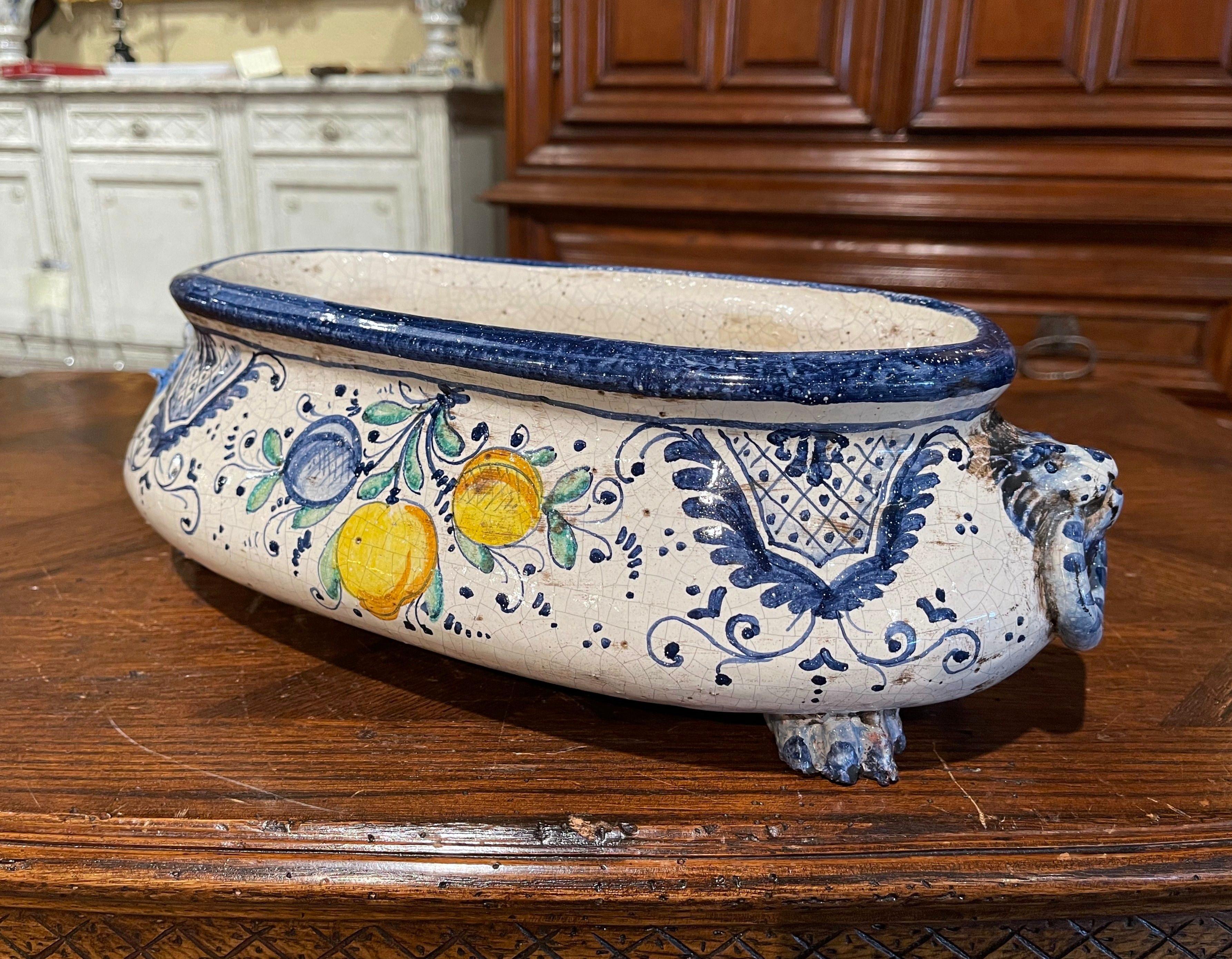 Decorate a buffet or dining table with this colorful ceramic cache pot. Crafted in France, circa 1920 and oval in shape, the jardinière stands on four paw feet and is dressed with lion head form handles. The faience planter is decorated with hand