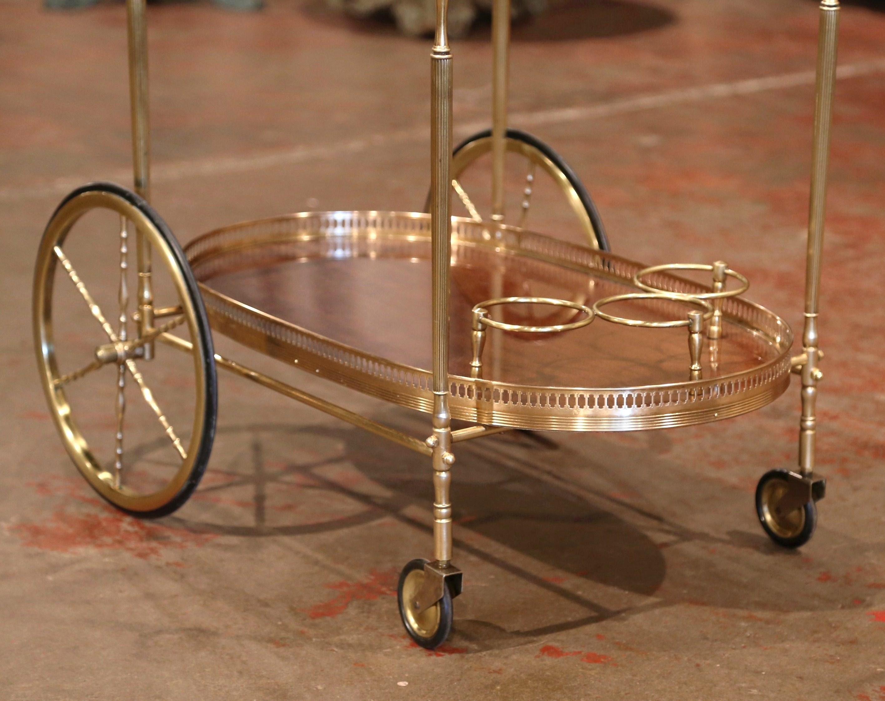 This elegant, vintage rolling bar cart was created in France, circa 1930. The large desert table with large front wheels and rubber tires, features a brass frame with two oval plateaus, one topped with glass surface, and the bottom with mahogany.