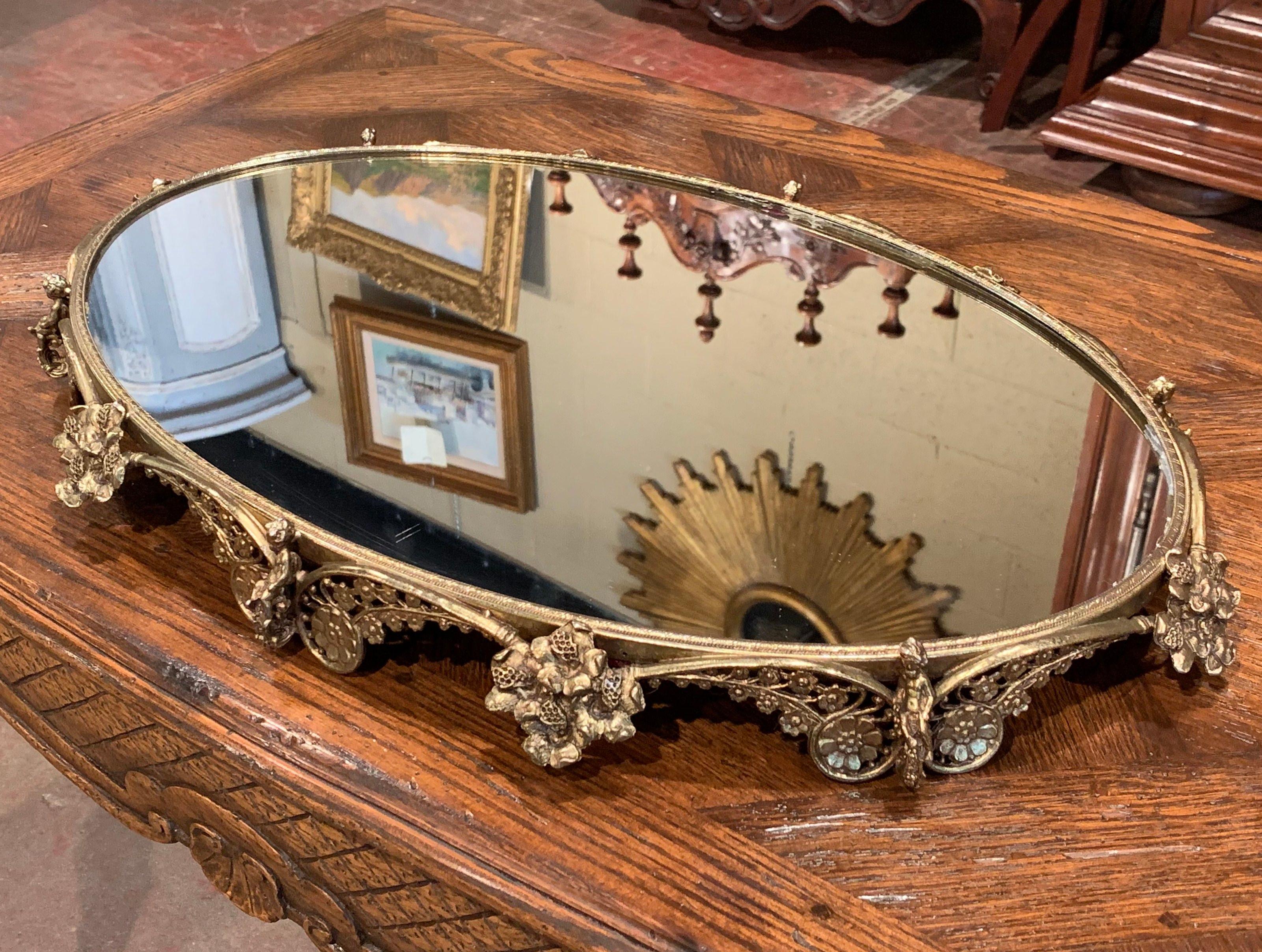 This large, elegant brass centerpiece was crafted in France, circa 1920. The antique, oval table plateau stands on small feet and features a scrolled frame of raised floral and cherub repousse decor. The platter with mirrored surface is in excellent