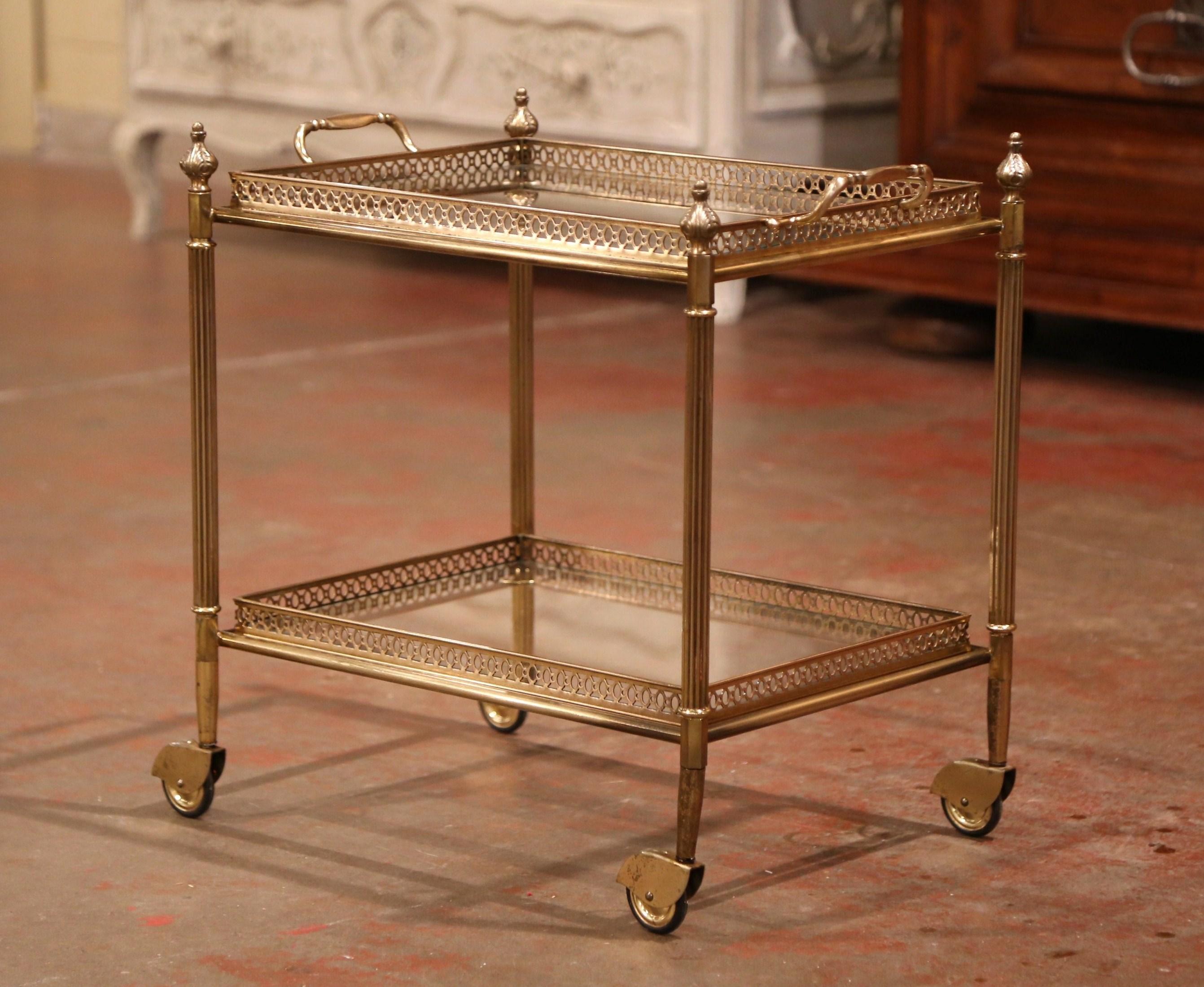 This elegant, vintage rolling bar cart was created in France, circa 1930. The desert table stands on four straight legs over small wheels and embellished with intricate cone finials at the top. The brass frame features two rectangular plateaus