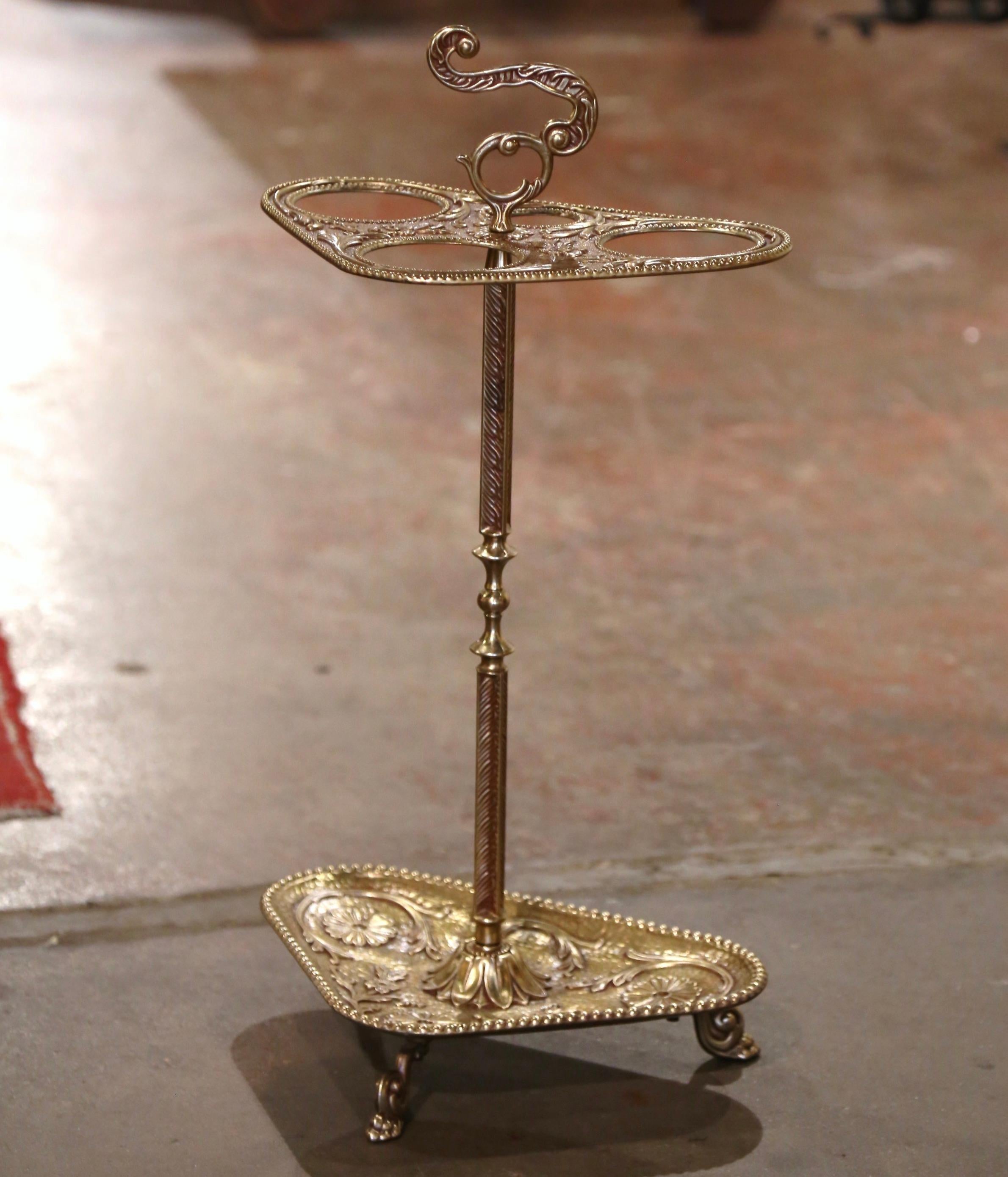 Decorate an entry with this elegant antique umbrella and cane stand. Created in France circa 1920 and built of brass, the piece stands on paw feet over a droplet tray decorated with repousse floral and leaf motifs. The top dressed with an intricate