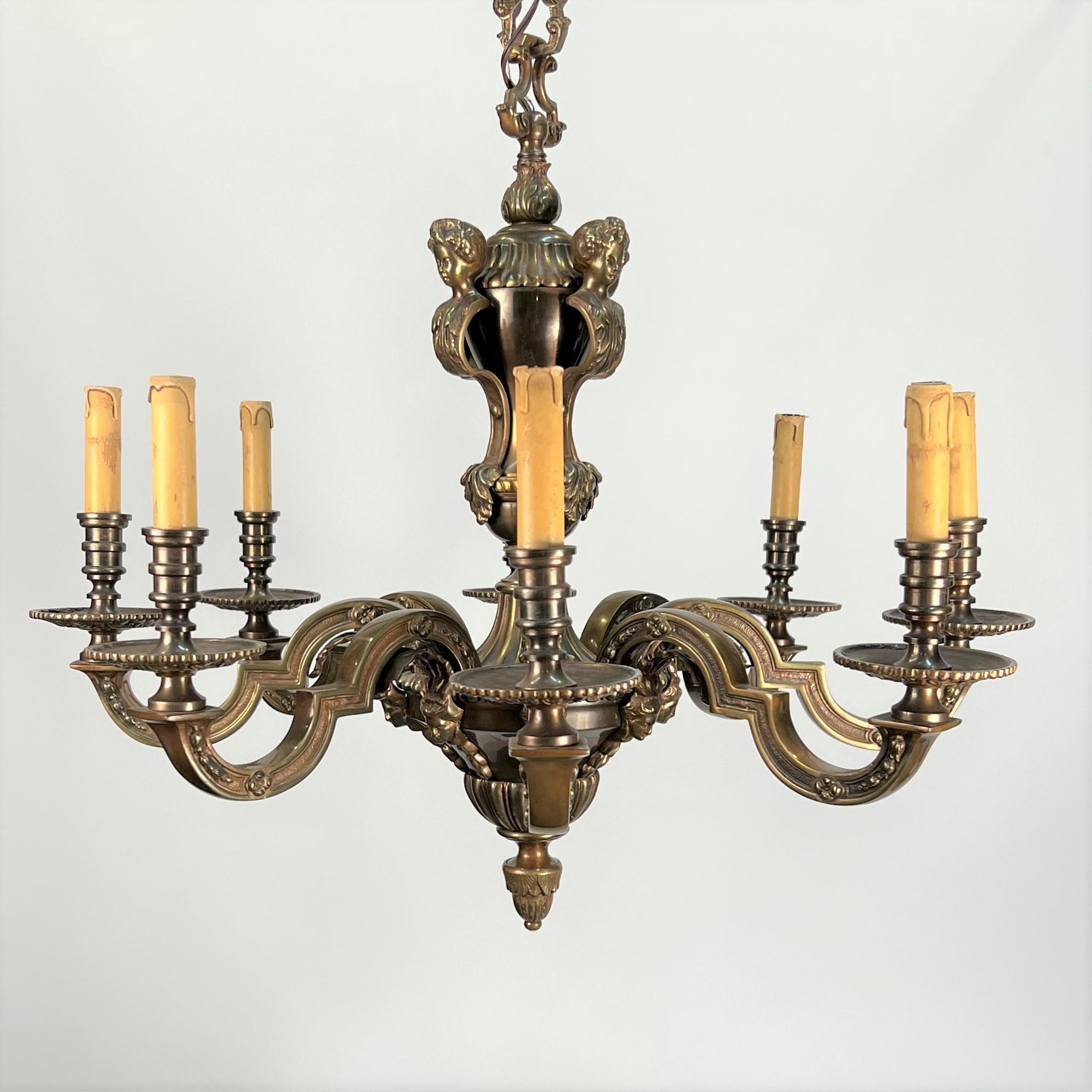 This early 20th century French bronze chandelier features female heads liking to the caryatides of the Acropolis. Each of the four heads at the top of the chandelier preside over eight beautifully hand cast and chased arms featuring bell flowers and