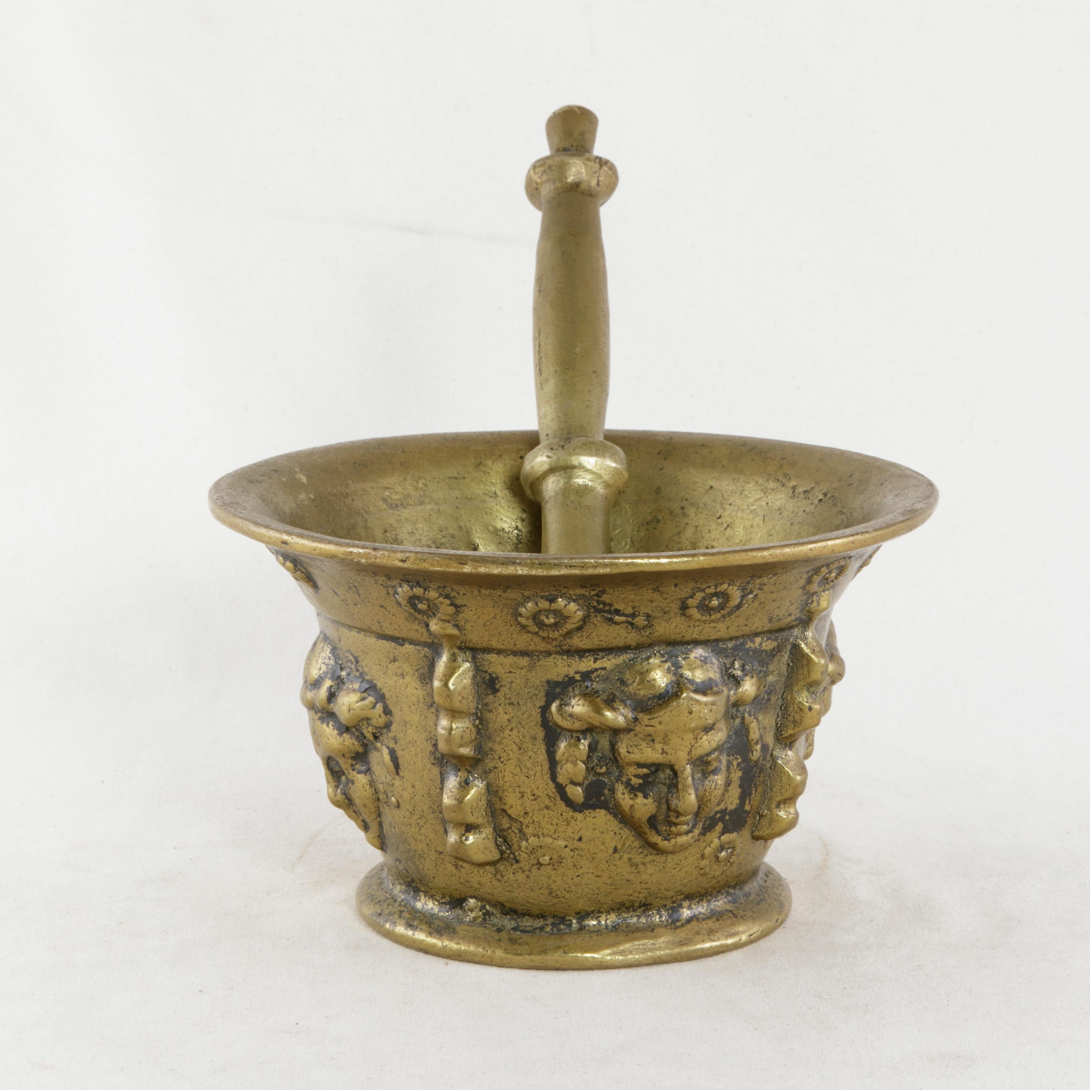 This French solid bronze mortar from the turn of the 20th century boasts its original eleven inch long bronze pestle. Its exterior is detailed with four masks and an upper ring of flowers. Originally used in a pharmacy, circa 1900.
