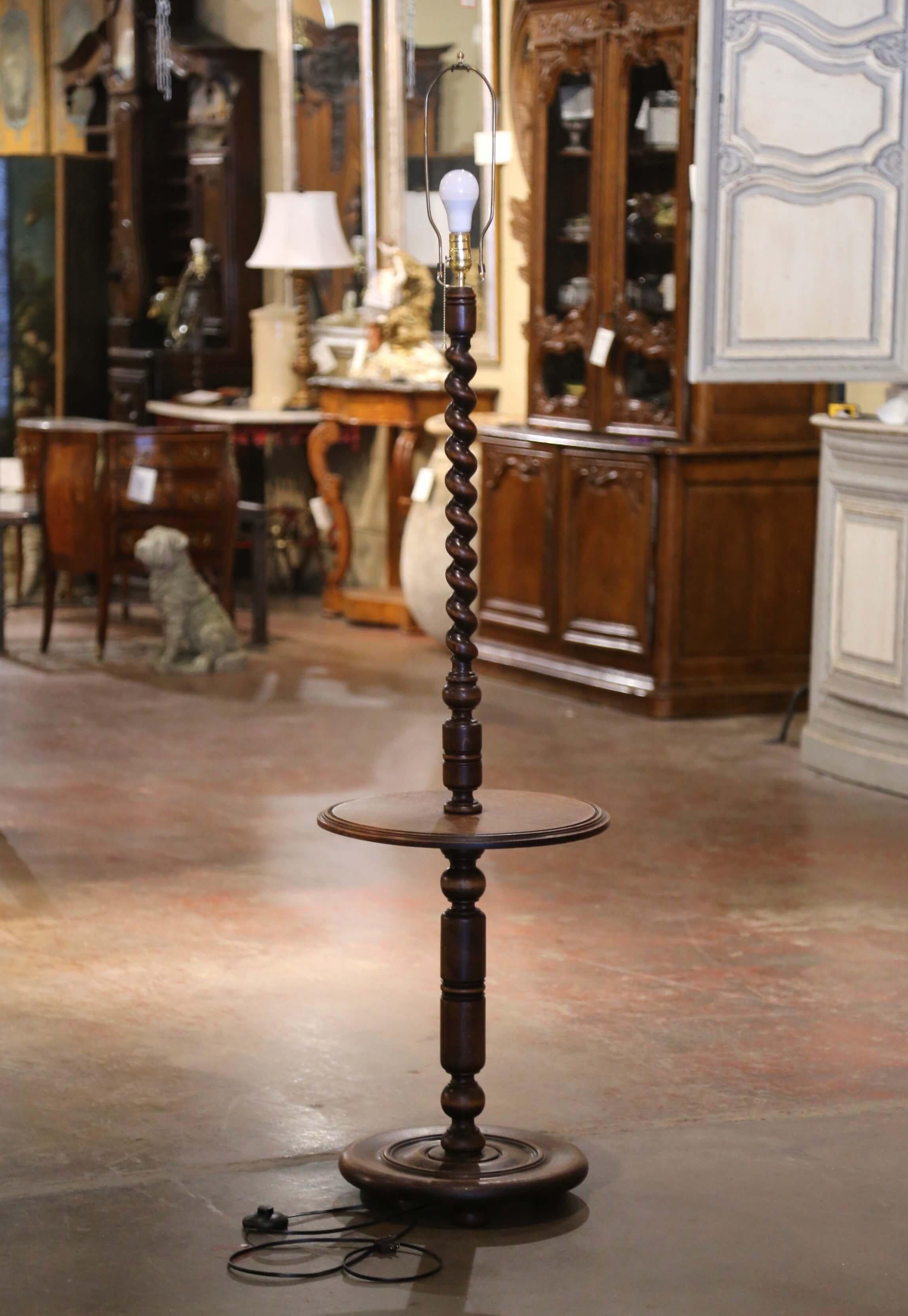 Esta singular lámpara de pie antigua se fabricó en el norte de Francia, hacia 1920. Apoyada en tres pies de bollo sobre una base circular, la lámpara ostenta un vástago retorcido de cebada, con una superficie central de saliente redondo que presenta