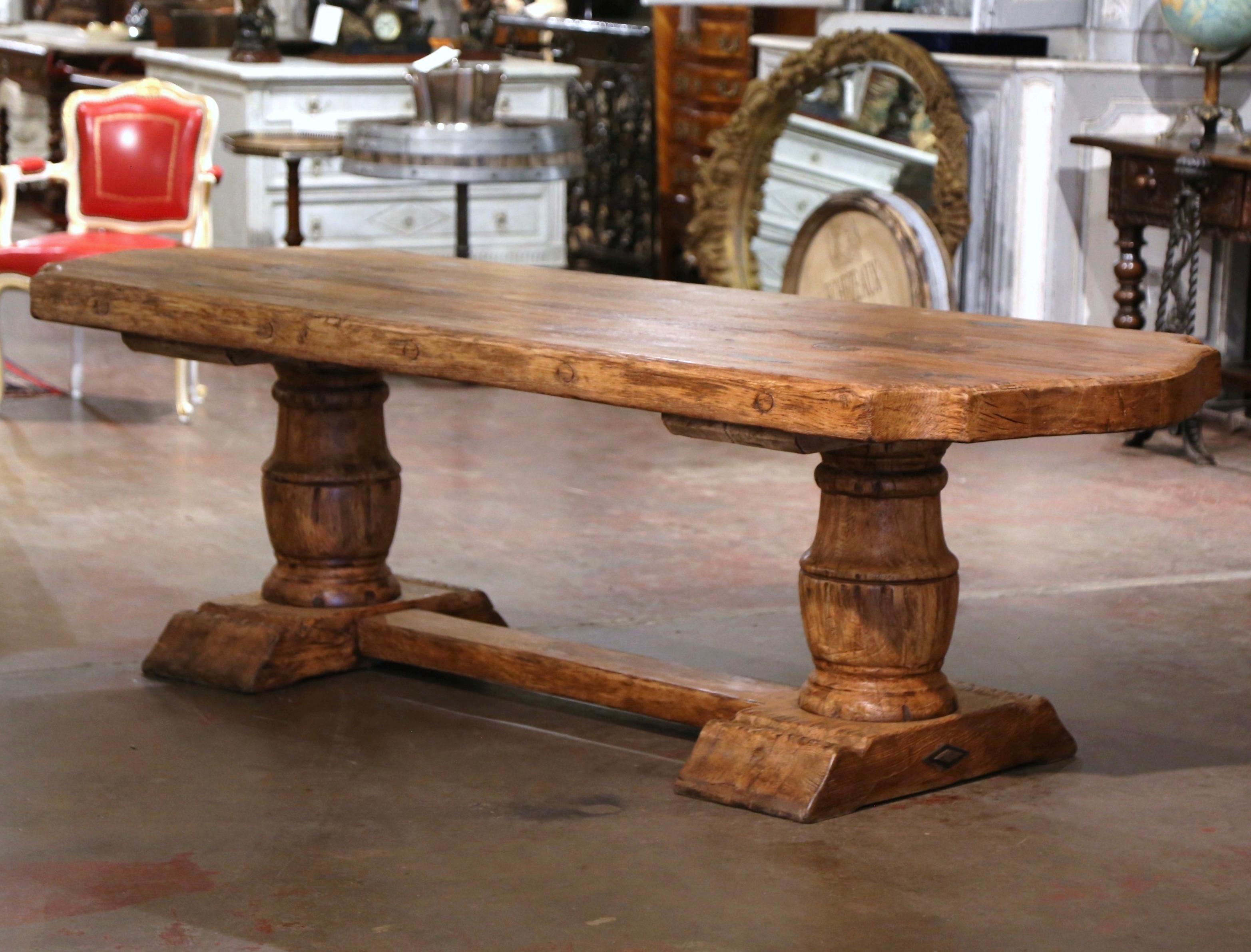 This elegant antique dining table was crafted in Normandy, France circa 1920. Built of solid oak, the rustic table stands on two substantial carved baluster-form support legs ending with molded shoe base, and joined by cross stretcher. The pedestal