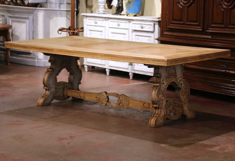 This elegant and large antique dining room table was crafted in France, circa 1920. Standing on a trestle base with two carved scrolled pedestal legs decorated with foliage motifs and connected with a pierced cross stretcher, the Louis XIII style