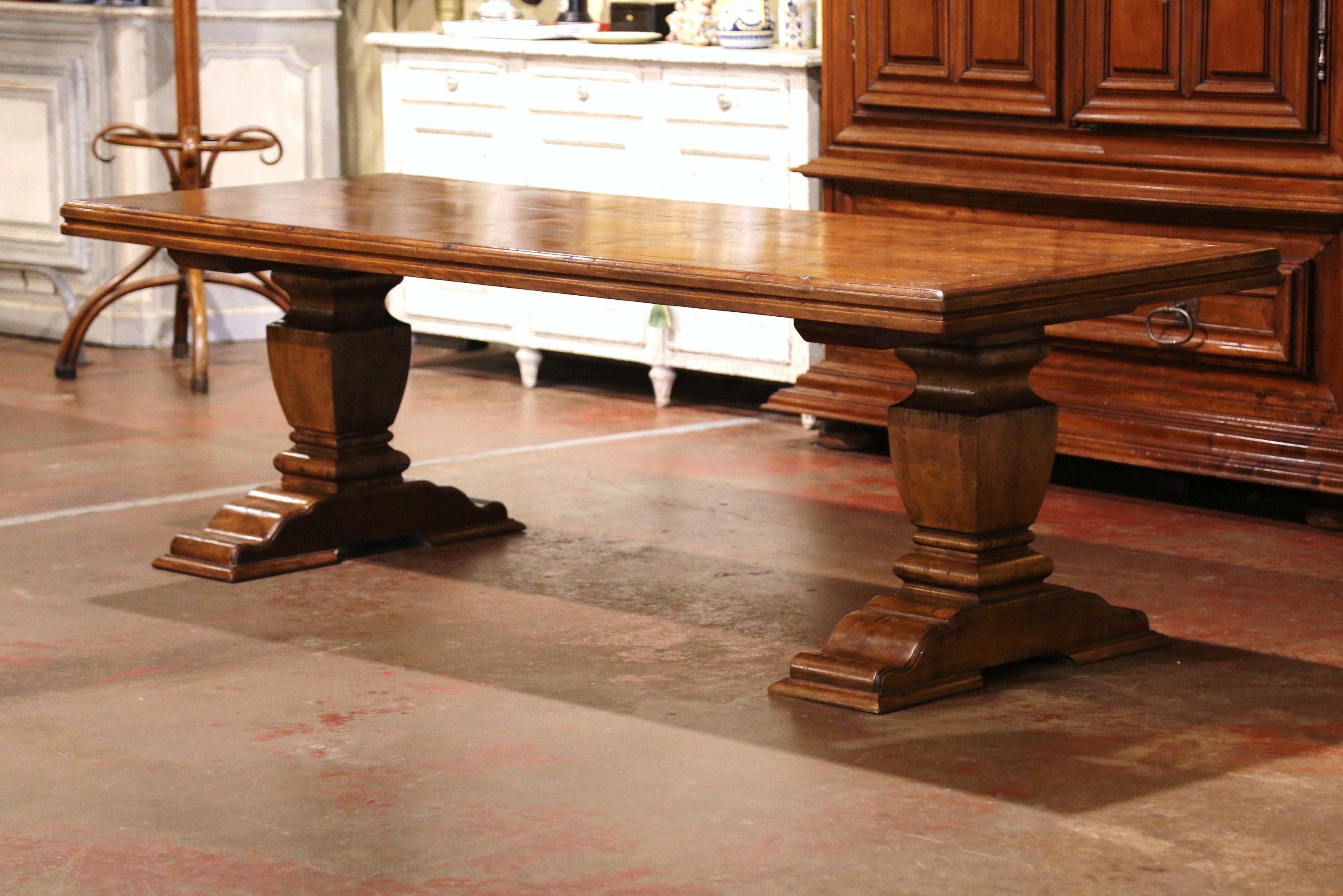 This elegant and large antique dining table was crafted in France, circa 1920. Standing on a massive carved double supports ending with shoe base, the Louis XIII style table is dressed with a thick rectangular paneled top embellished with double