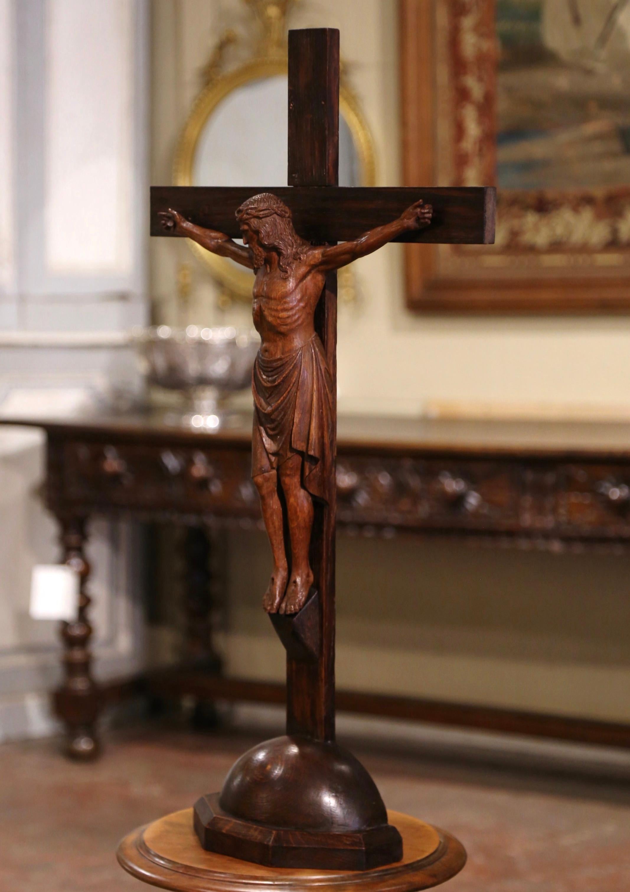Dieses freistehende antike Kreuz wurde in Frankreich von Hand aus Eichenholz geschnitzt. Das Kruzifix ist vom Künstler signiert und auf 1923 datiert und steht auf einem kugelförmigen Sockel.  und zeigt unseren an das Kreuz genagelten Herrn Jesus