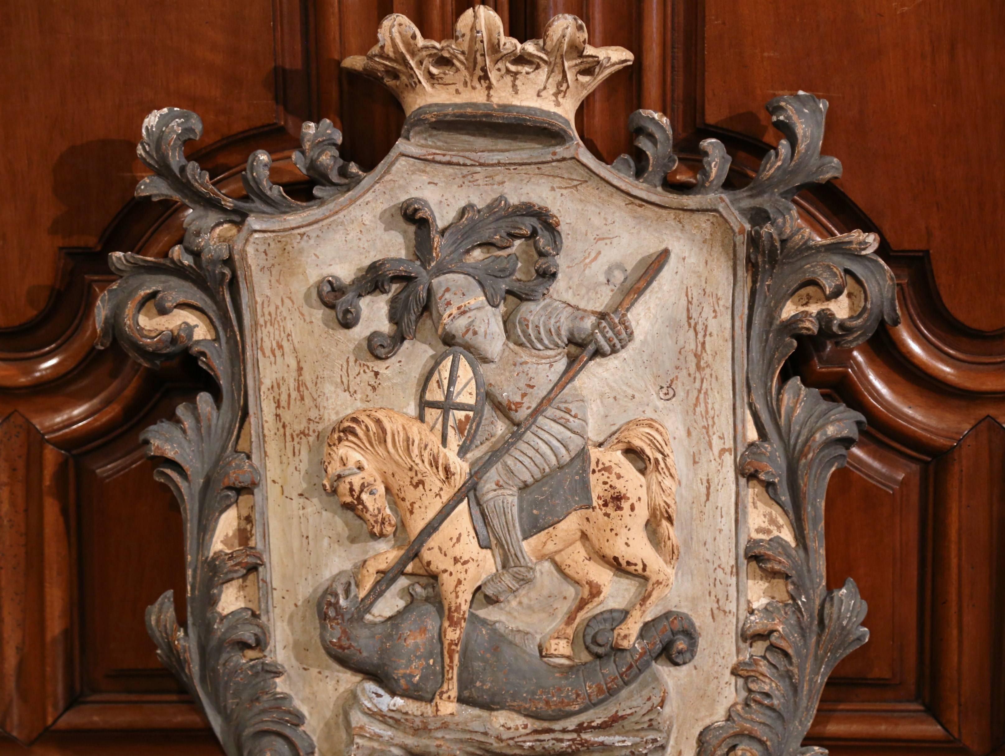 Embellish your wall with this large antique, medieval crest. Hand-carved in France, circa 1920, the traditional, painted shield has a crown at the pediment with decorative foliage motifs on both sides. The centre part features a warrior in full