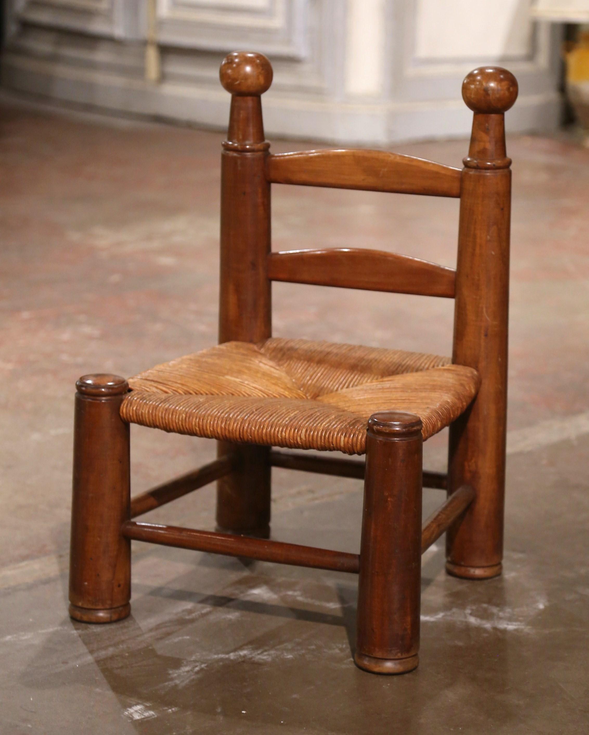 Cette très confortable chaise d'enfant ancienne à dossier en échelle a été fabriquée en Normandie, en France, vers 1940. Construite en bois de noyer et attribuée à Charles Dudouyt, la chaise repose sur des pieds ronds et tournés et présente deux