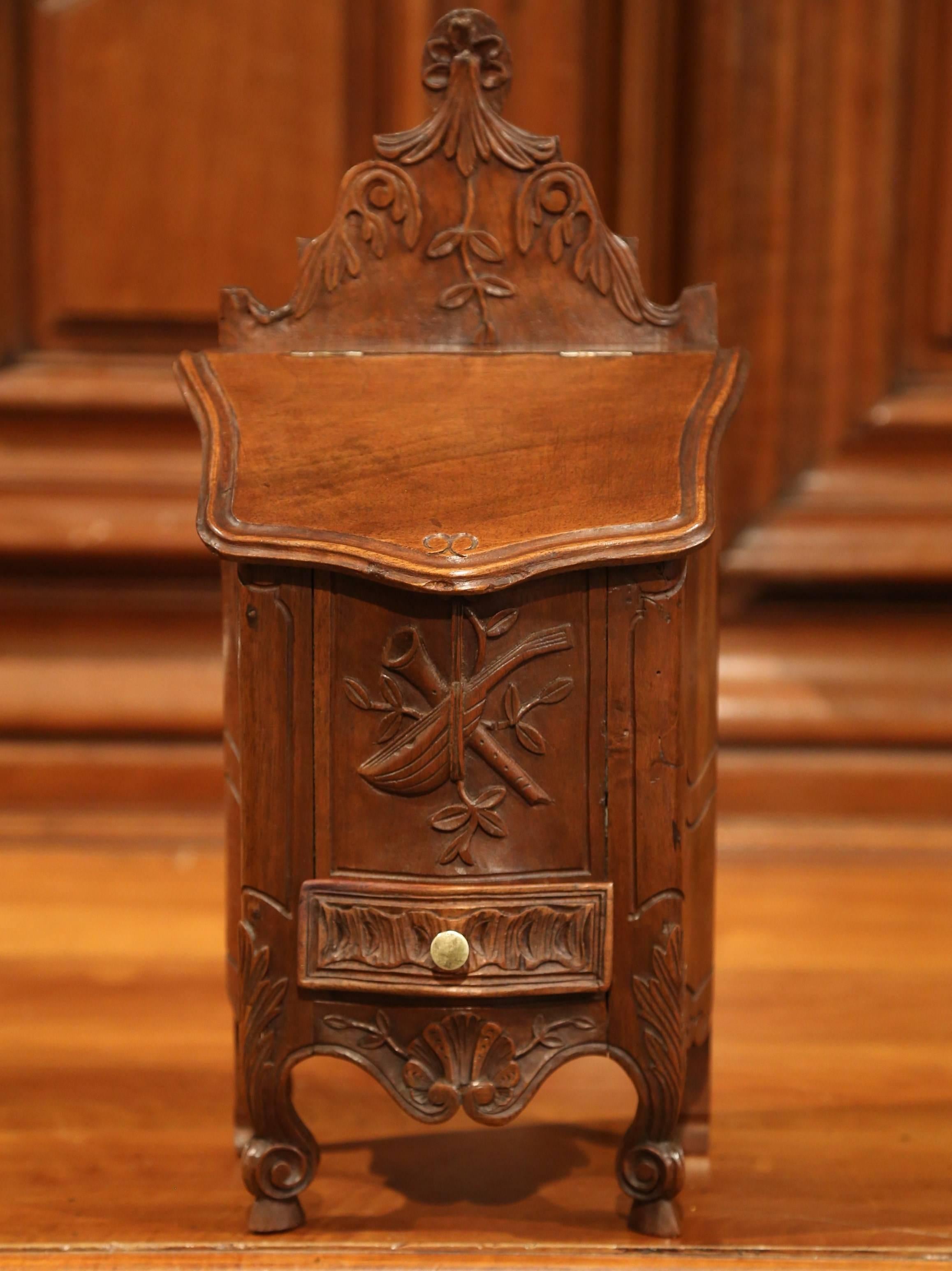 This elegant, antique fruitwood salt box was crafted in Avignon, France, circa 1920. The ornate walnut box features beautiful carved work throughout with music instruments and floral motifs, small scrolled feet, a usable drawer and an open top for