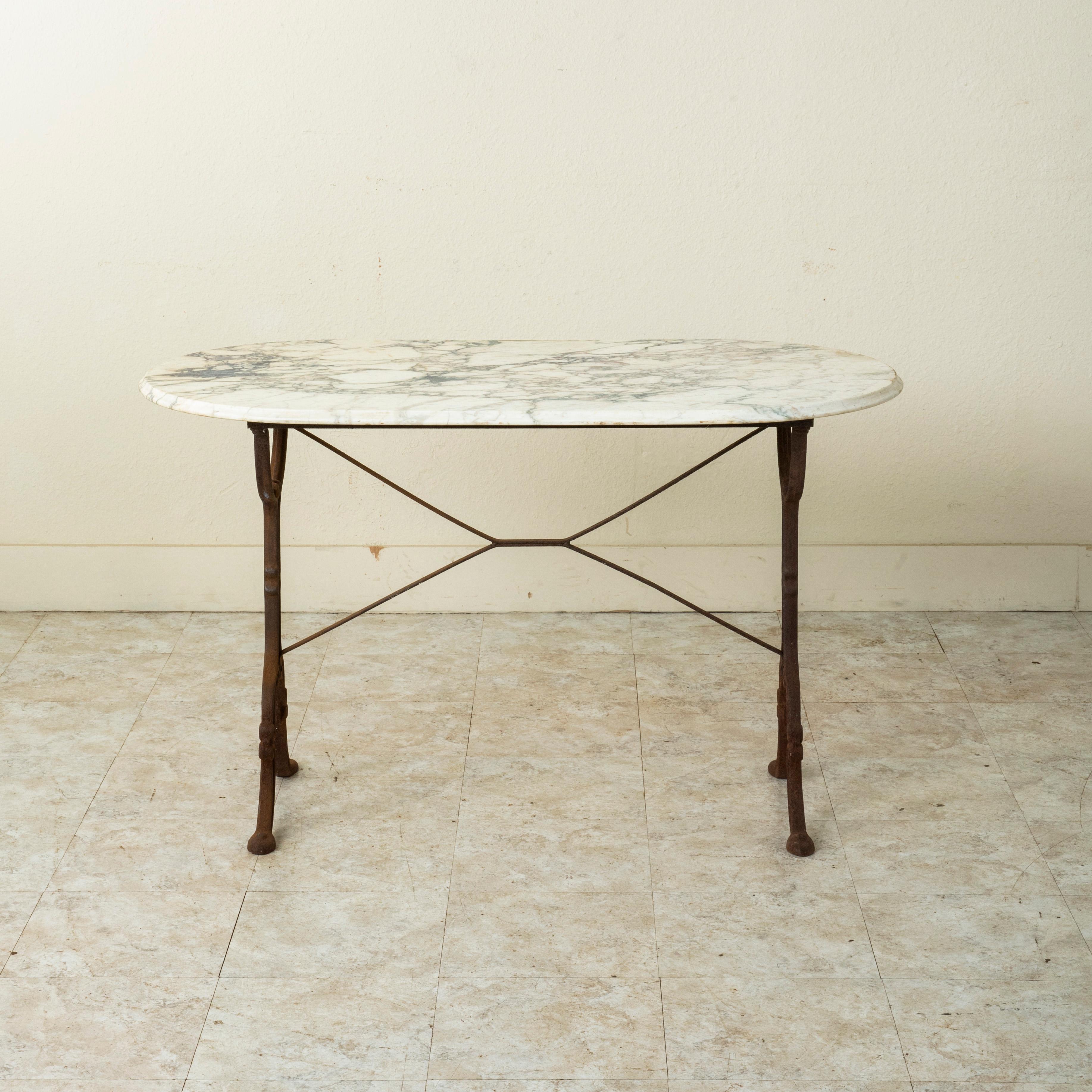 Originally used in a French brasserie from the turn of the twentieth century, this cast iron bistro table or cafe table features a solid beveled white marble top. Scrolled iron legs support the top and are joined by an X-stretcher that provides