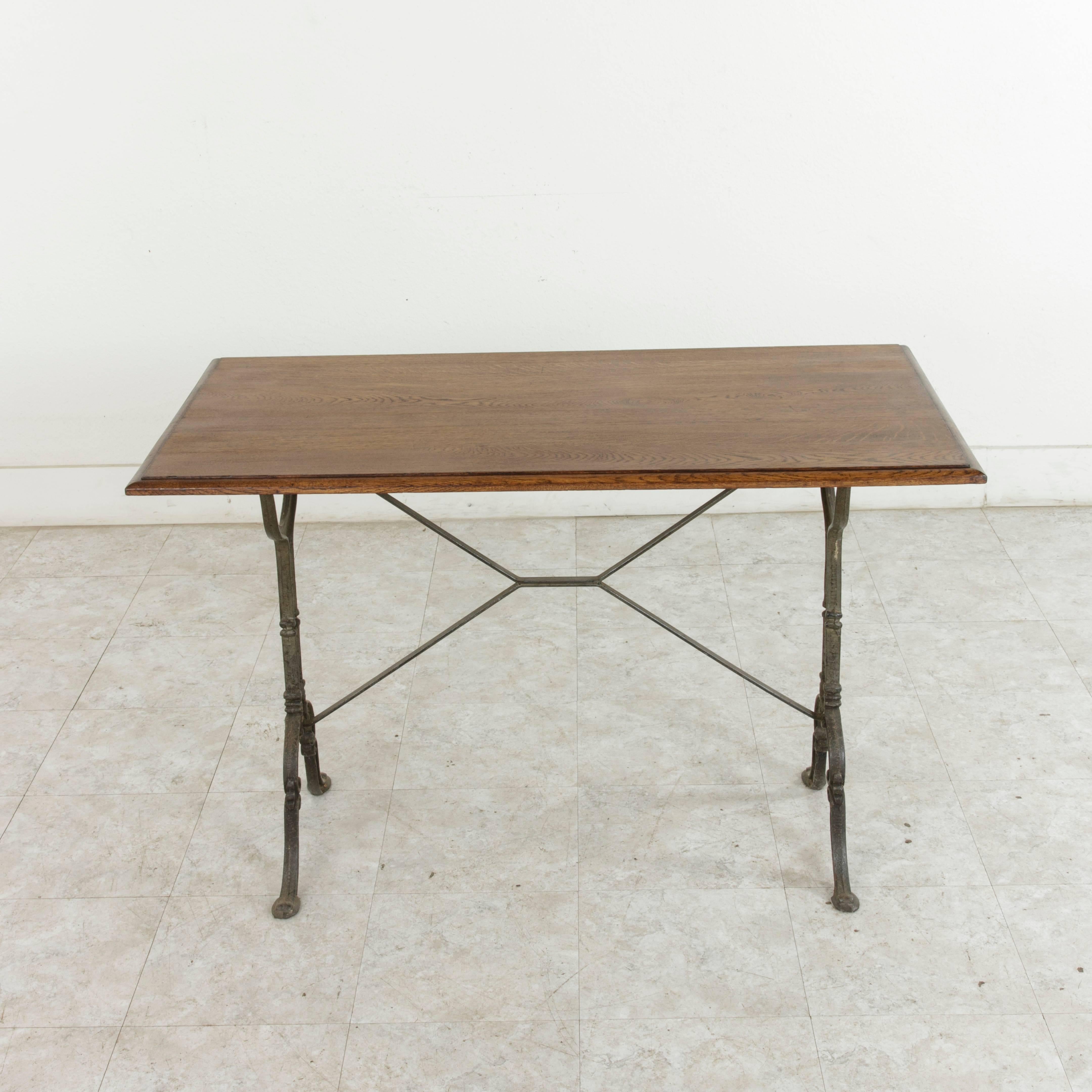 Originally used in a French brasserie in the early 20th century, this bistro table or cafe table features a cast iron base and a bevelled oak top. The classic scrolled iron legs of the piece are joined by an X-stretcher that provides additional