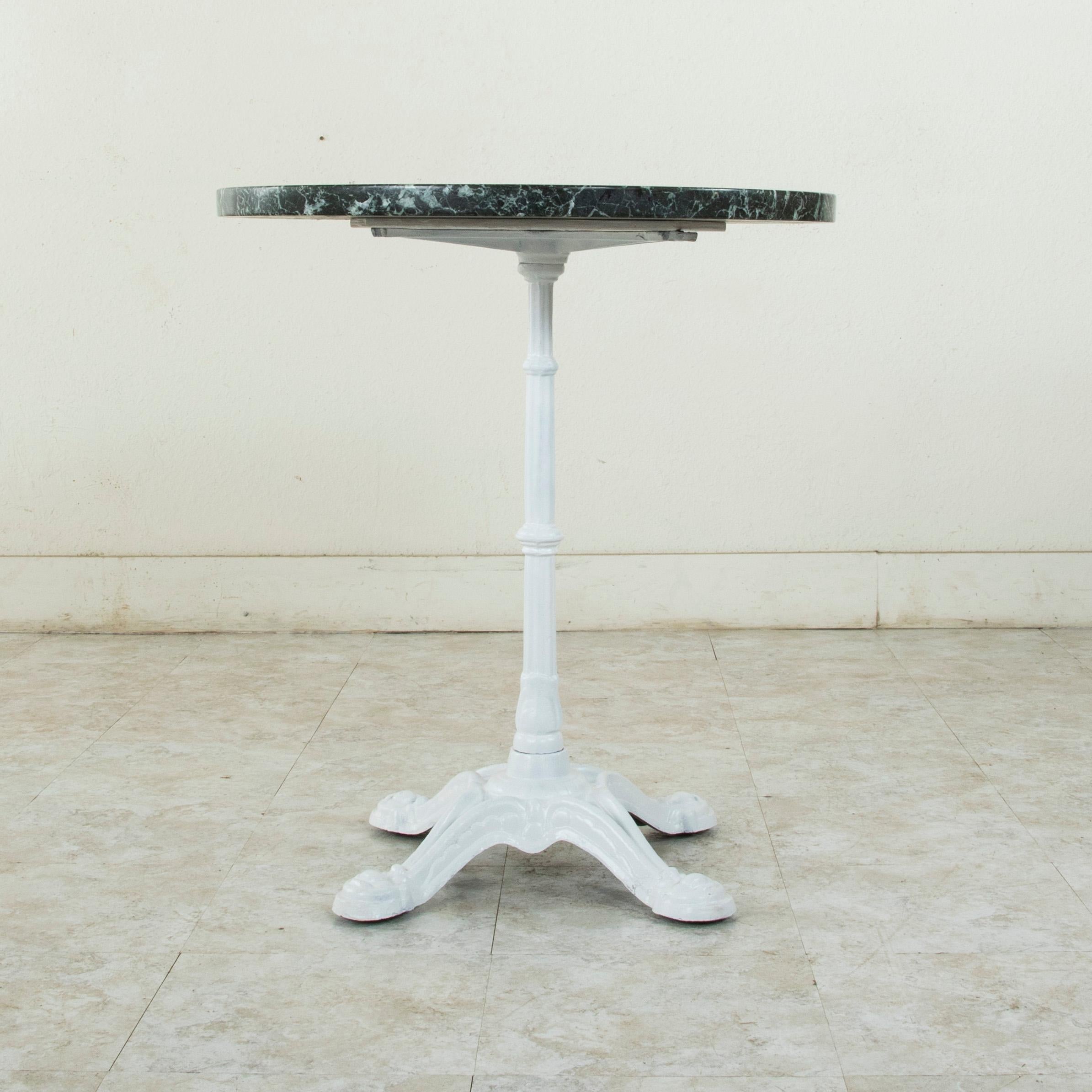 This early 20th century French bistro table features a cast iron base and a solid 1.25 inch thick circular green marble top with white veining. The marble top is supported by a central fluted pillar that rests on four legs. The marble sits on a